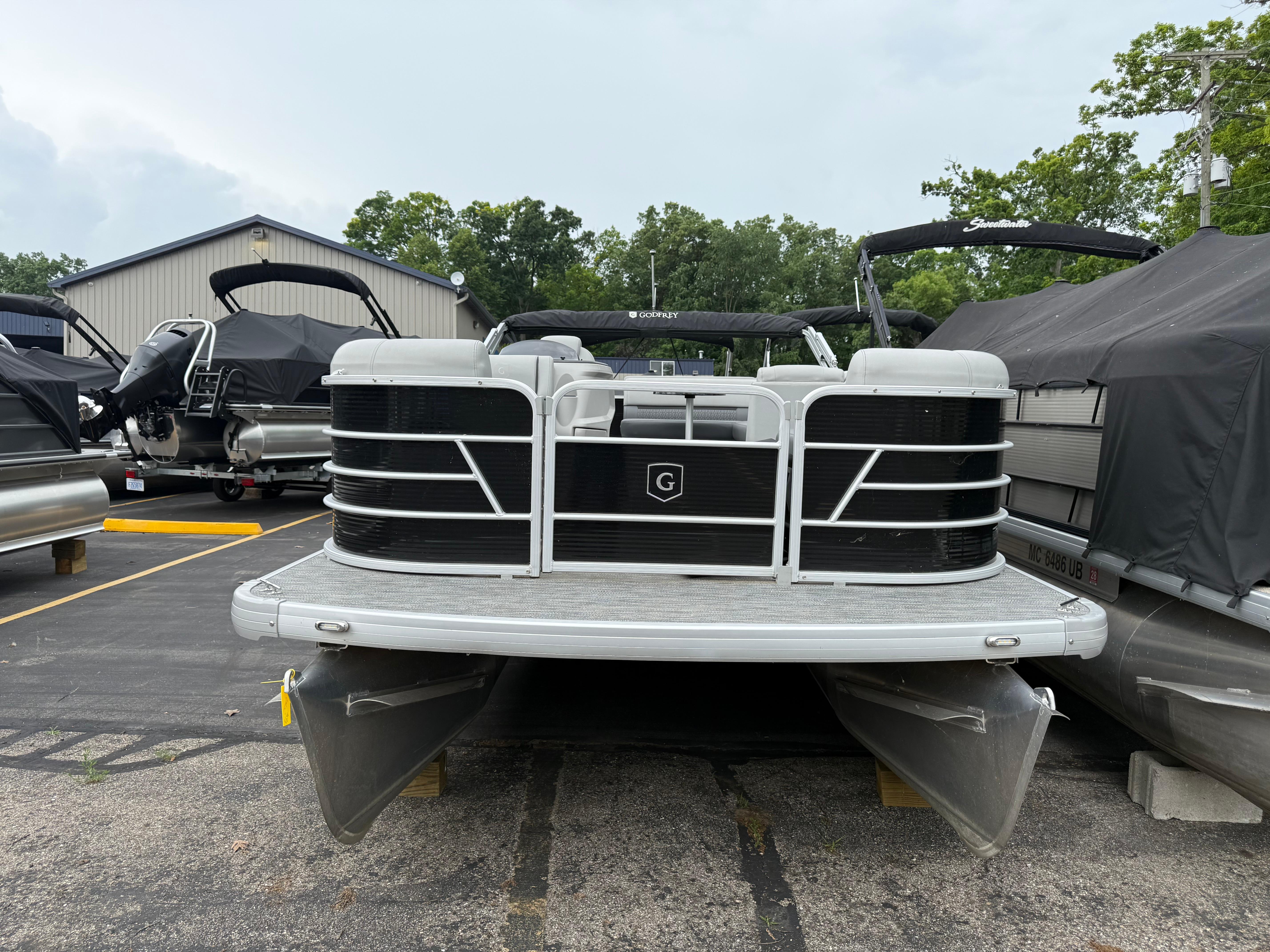 2023 Godfrey Sweetwater pontoon boat in a parking lot, surrounded by other boats.