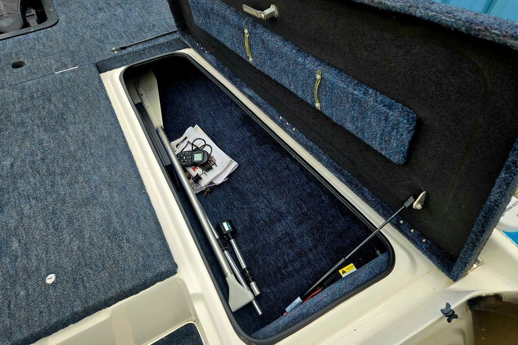 Open storage compartment in 1996 Champion 181 SX boat, showing equipment and blue carpeting.