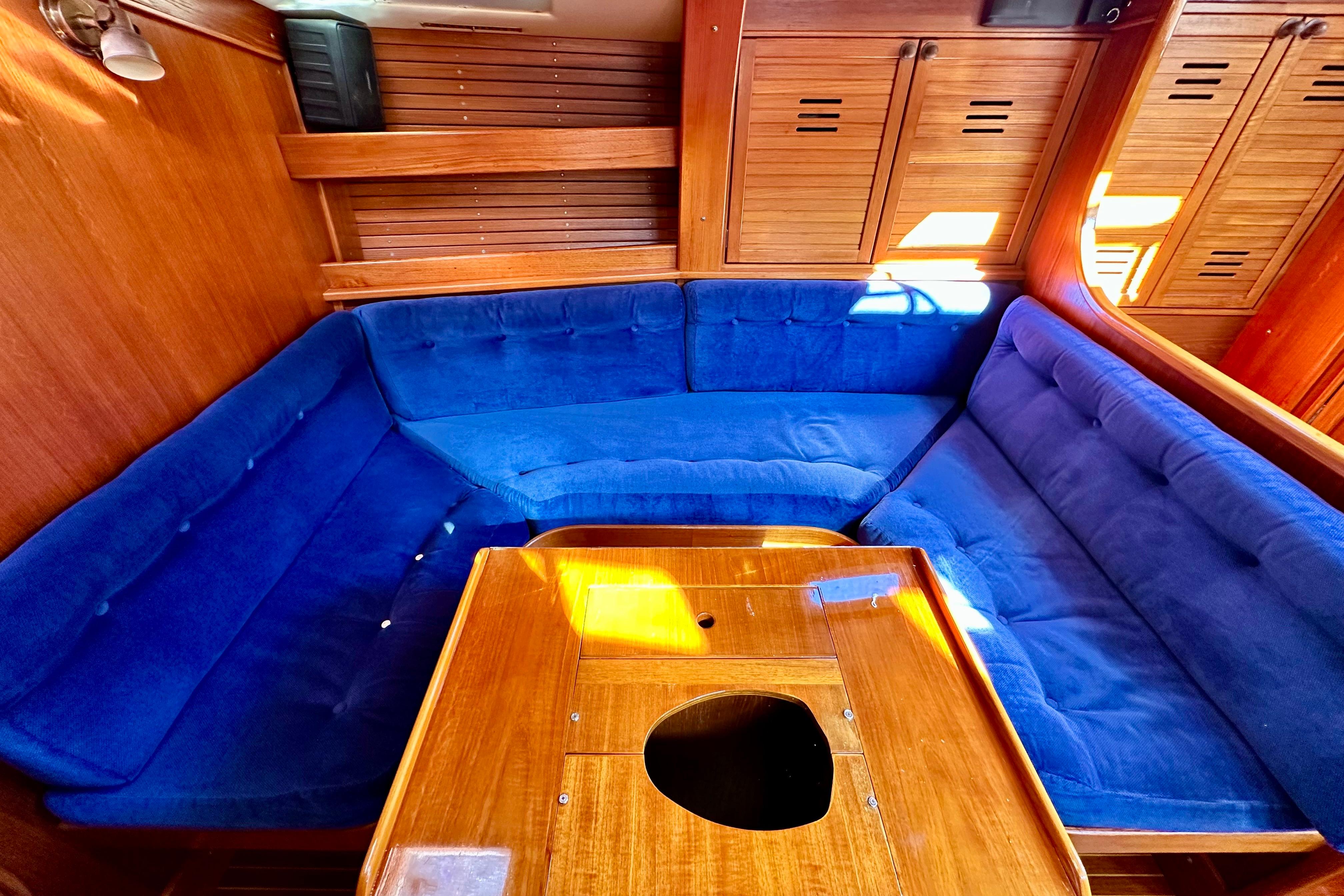 Interior of 1984 Jonmeri 40 yacht with blue cushioned seating and wooden table.
