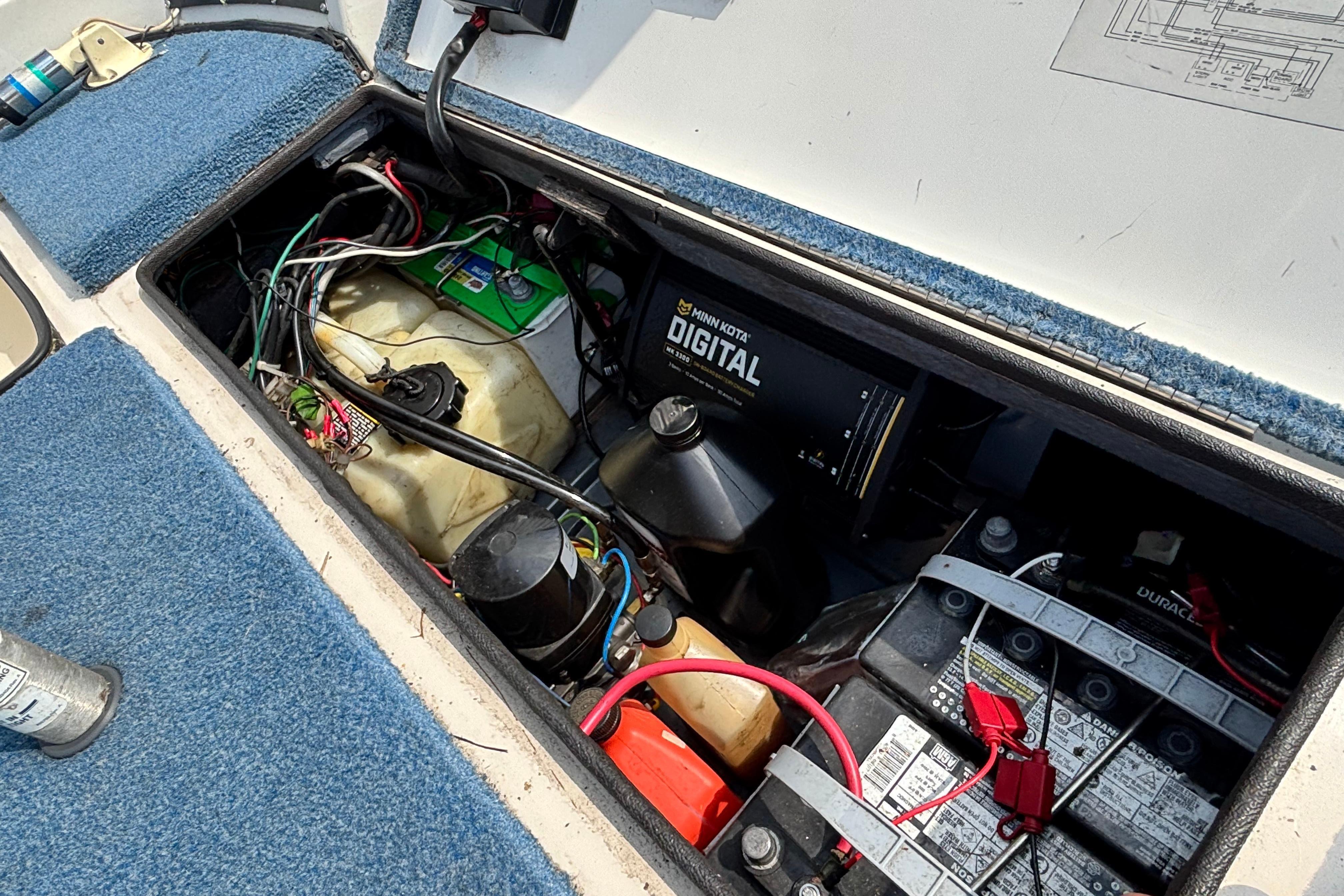 An open storage compartment reveals batteries and electronics on a boat with blue carpeting.