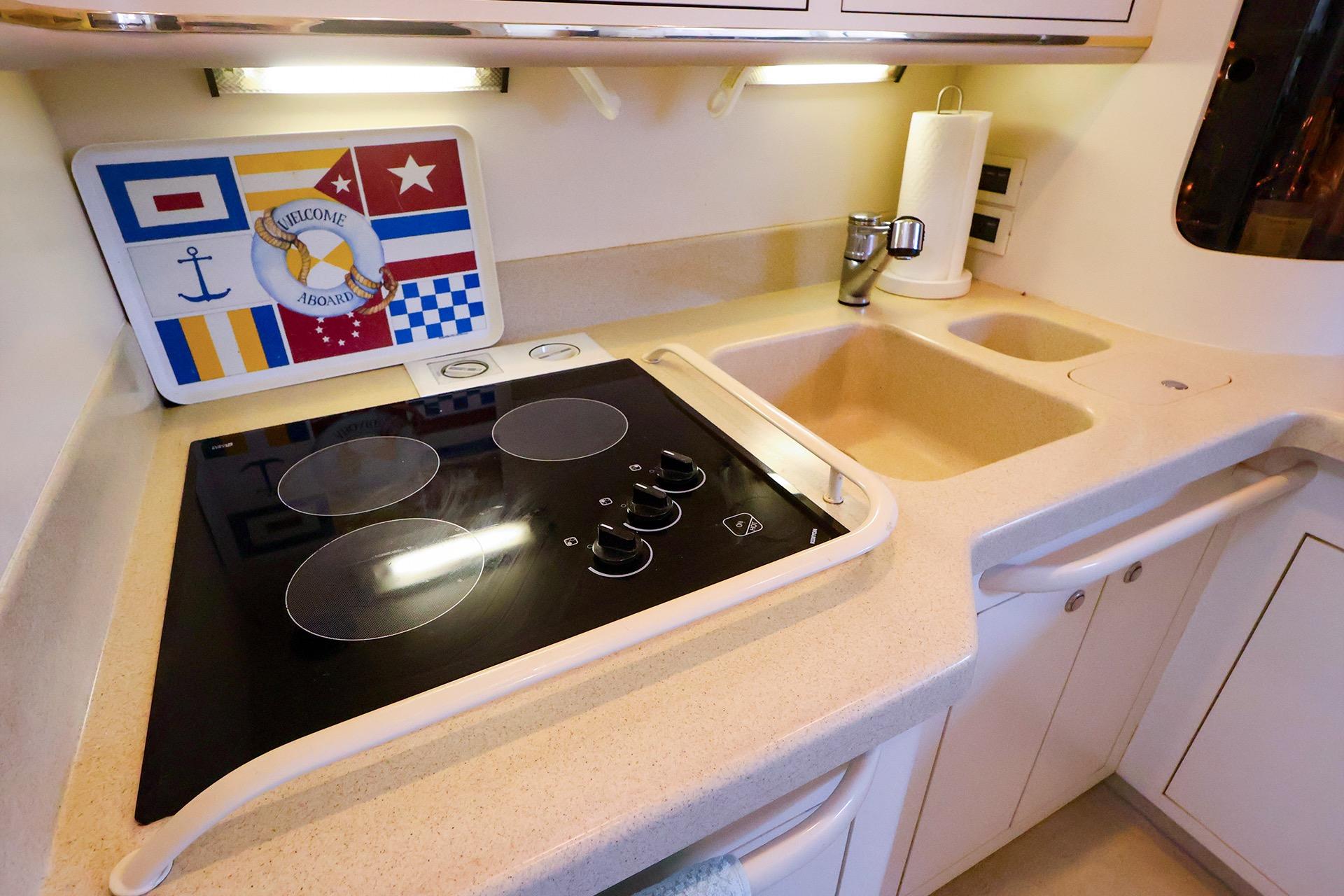1998 Sea Ray 500 Sundancer kitchen with electric stove, sink, and nautical decor.