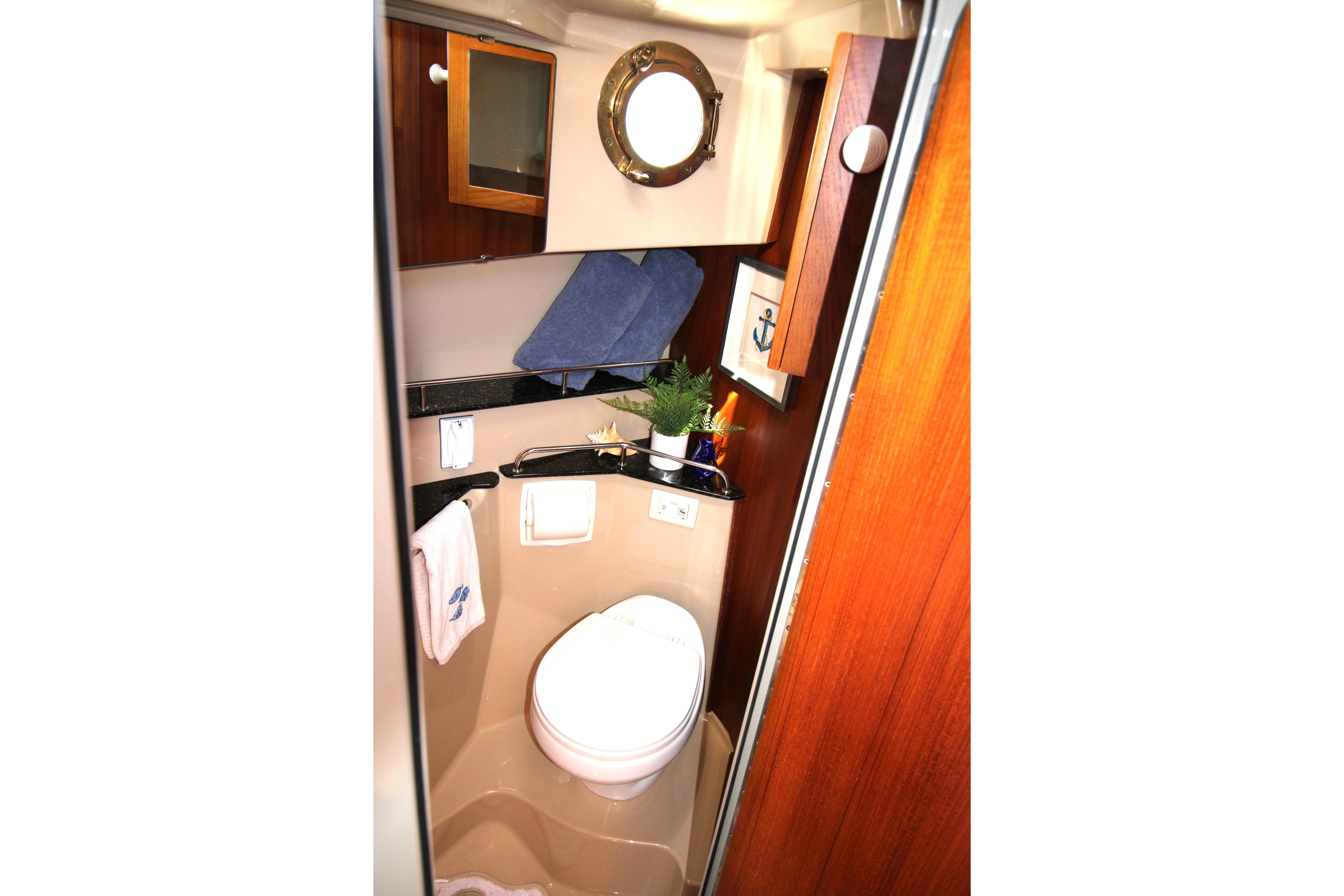 Compact bathroom in 2013 Ranger Tugs R-31 CB boat with porthole and wooden cabinetry.