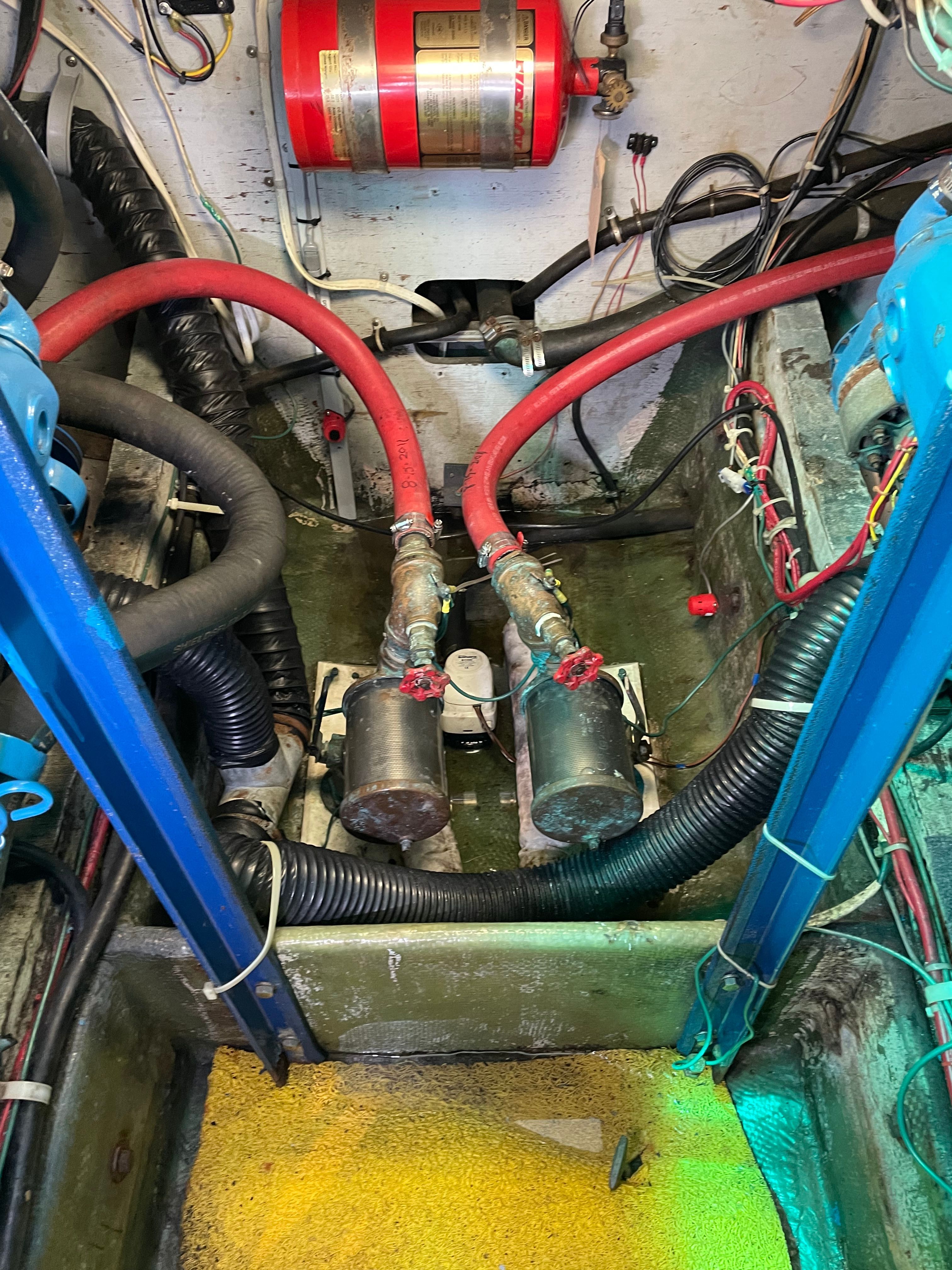 Engine room of a 1969 Bertram Caribe with hoses and fire extinguisher.