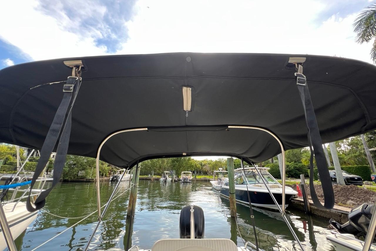 2016 Boston Whaler 170 Dauntless boat with canopy, docked in a scenic marina.