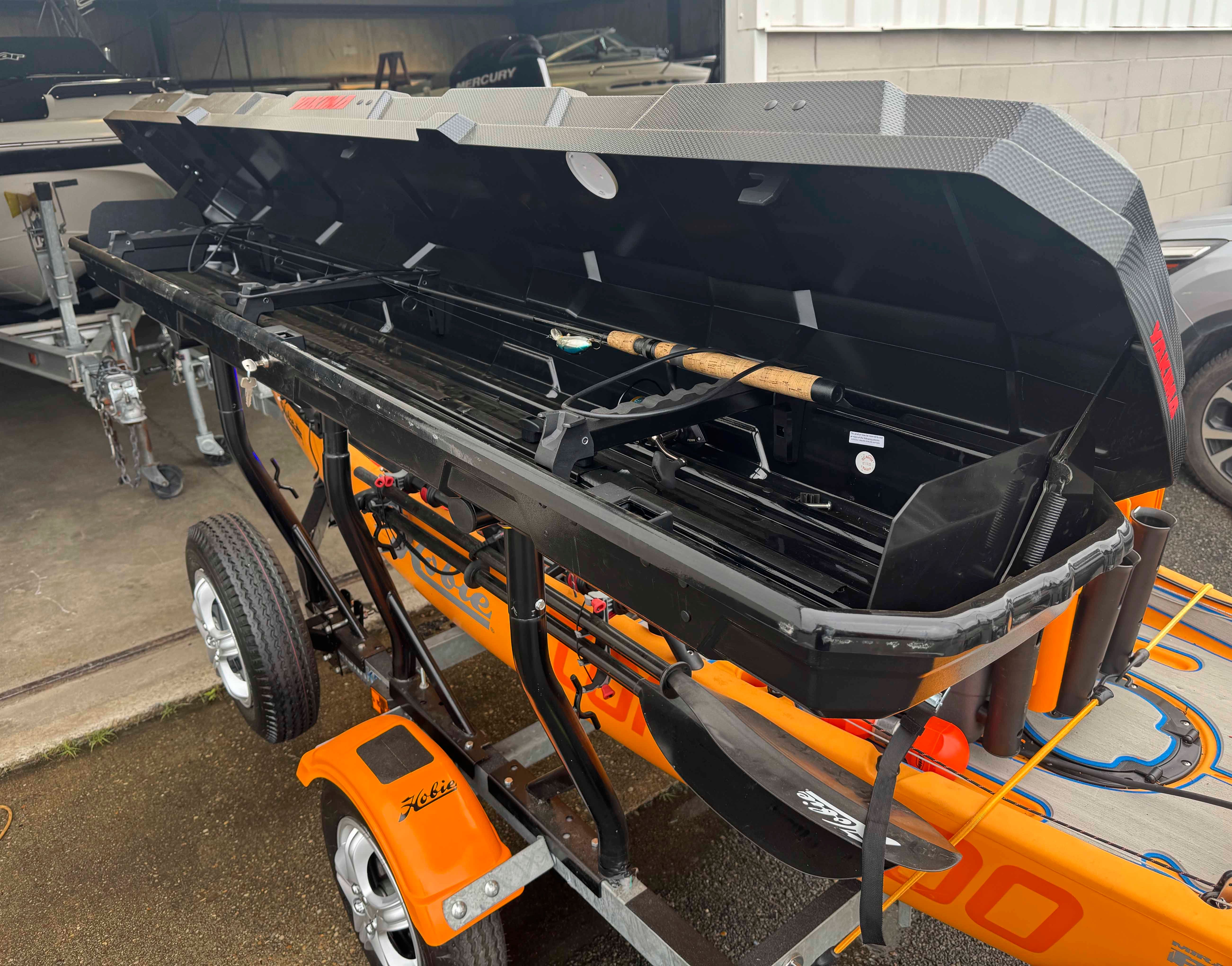 An orange Hobie 14 Pro Angler Kayak on a trailer with open storage compartment.