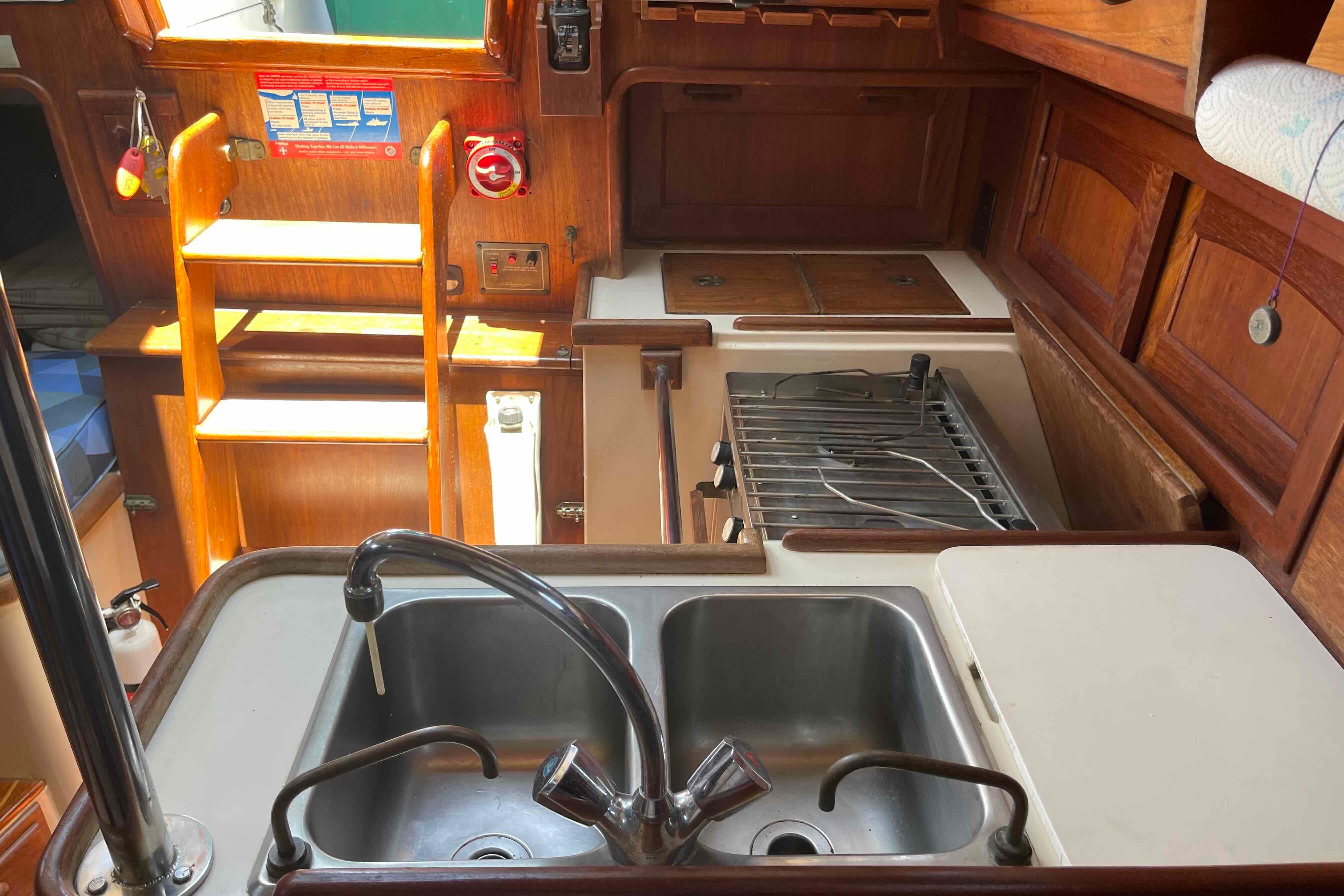 Interior of 1987 Pacific Seacraft 34 sailboat galley with sink, stove, and wooden cabinetry.