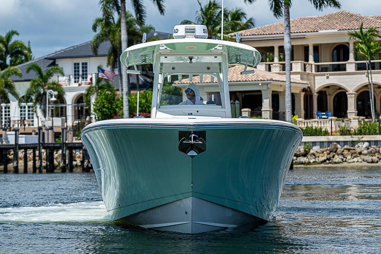 2019 Cobia 320 Center Console boat cruising near luxury waterfront homes.