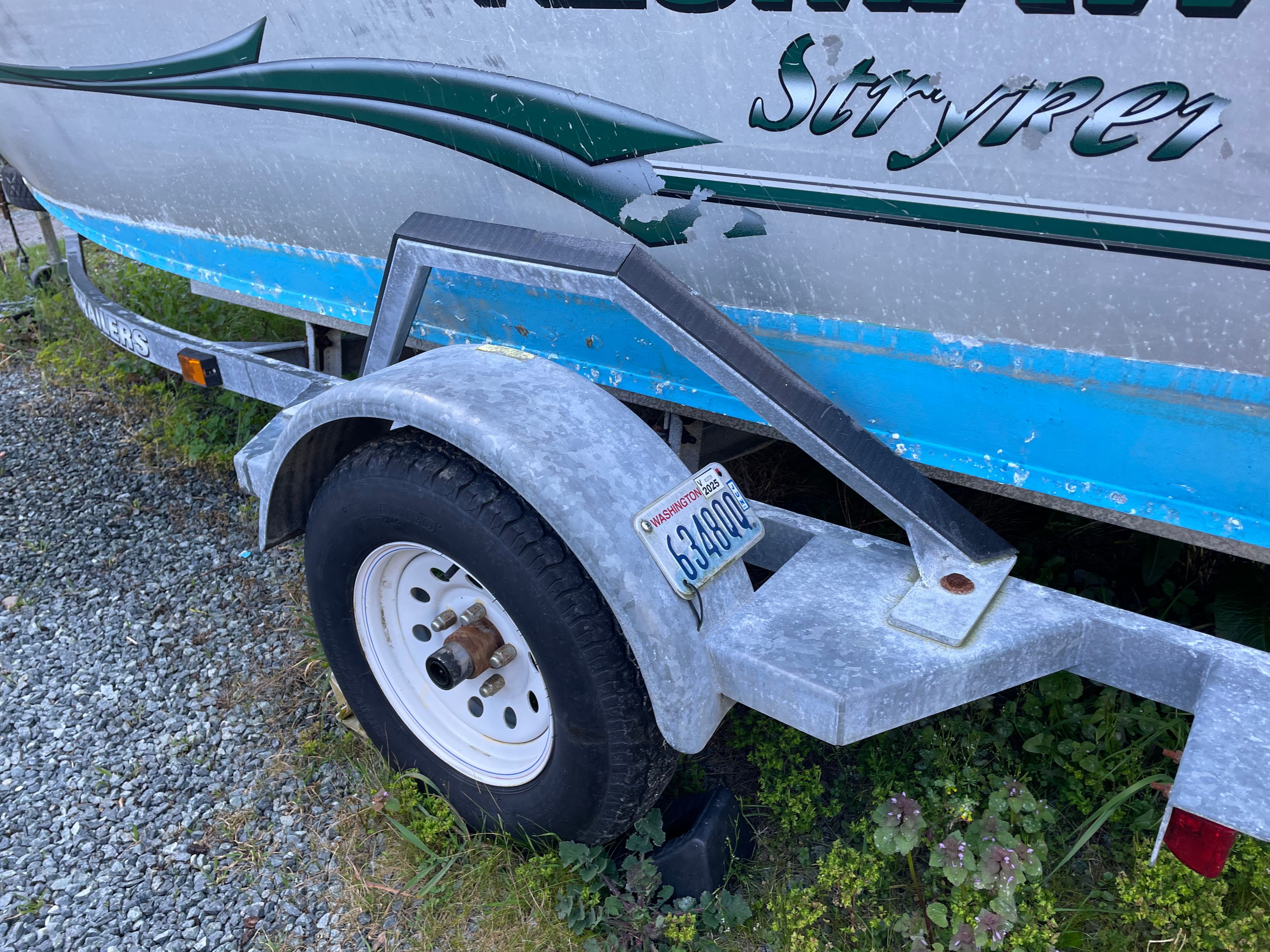 A 2001 Alumaweld Stryker boat on a trailer, parked on a gravel path.