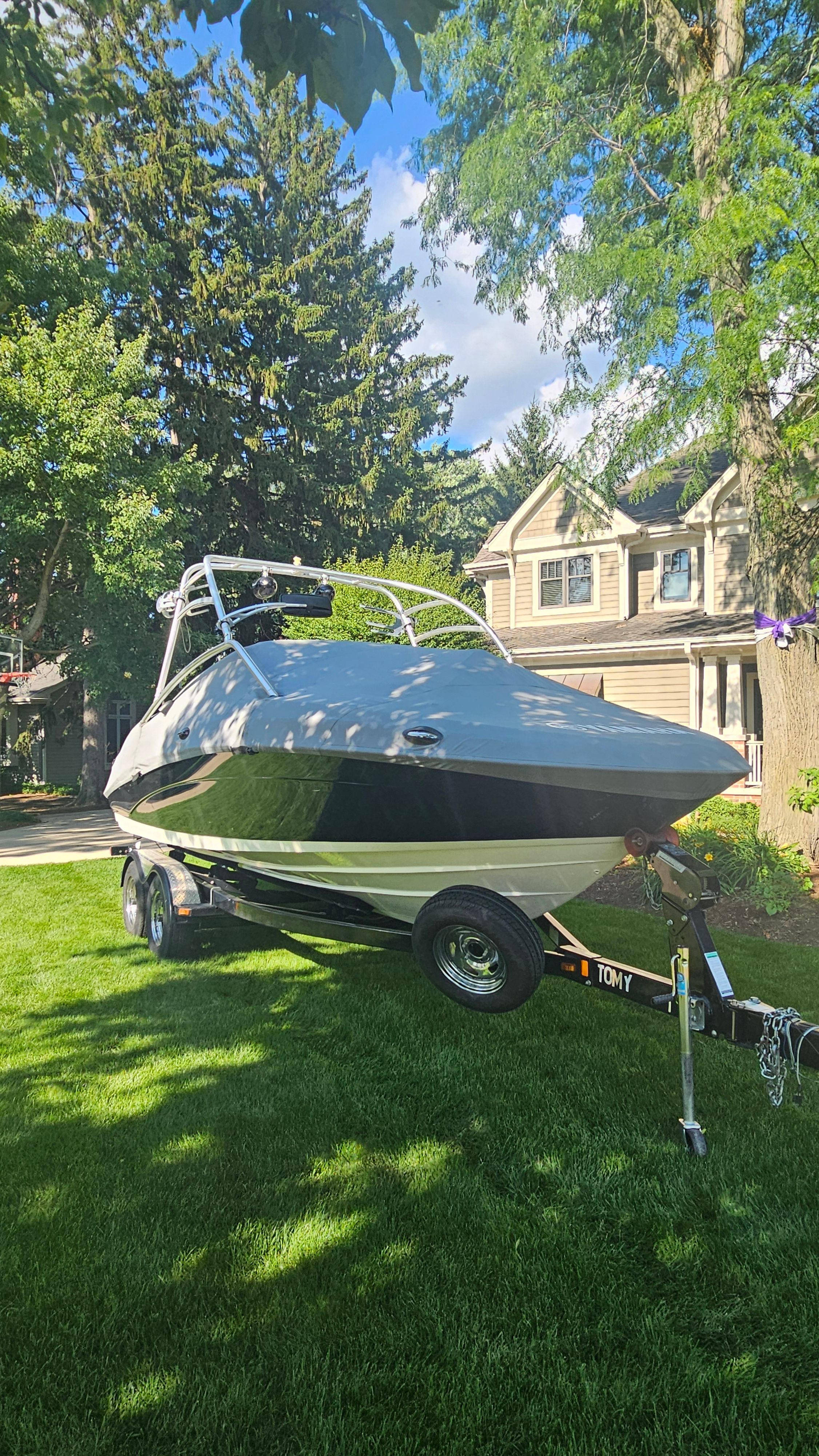 A 2010 Yamaha AR210 boat on a trailer in a garden, surrounded by trees.