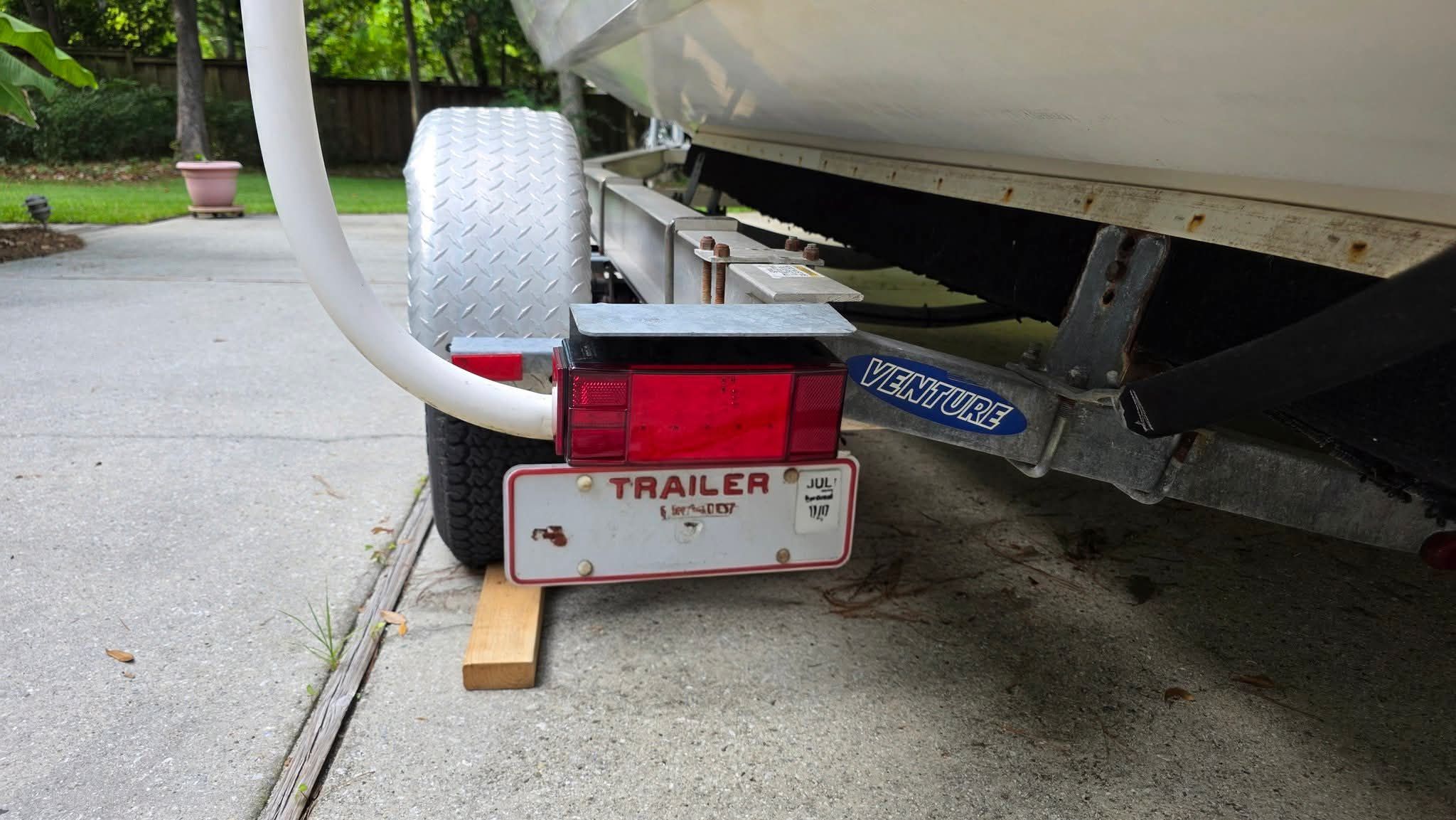 A boat trailer with a license plate and taillight, supported by a wooden block.