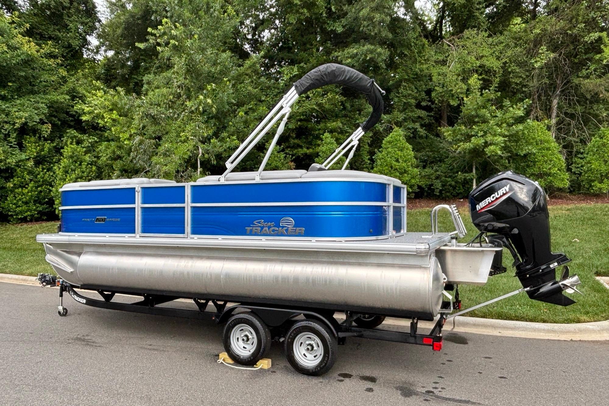 2026 Sun Tracker Party Barge 20 DLX pontoon boat on trailer, parked near lush greenery.