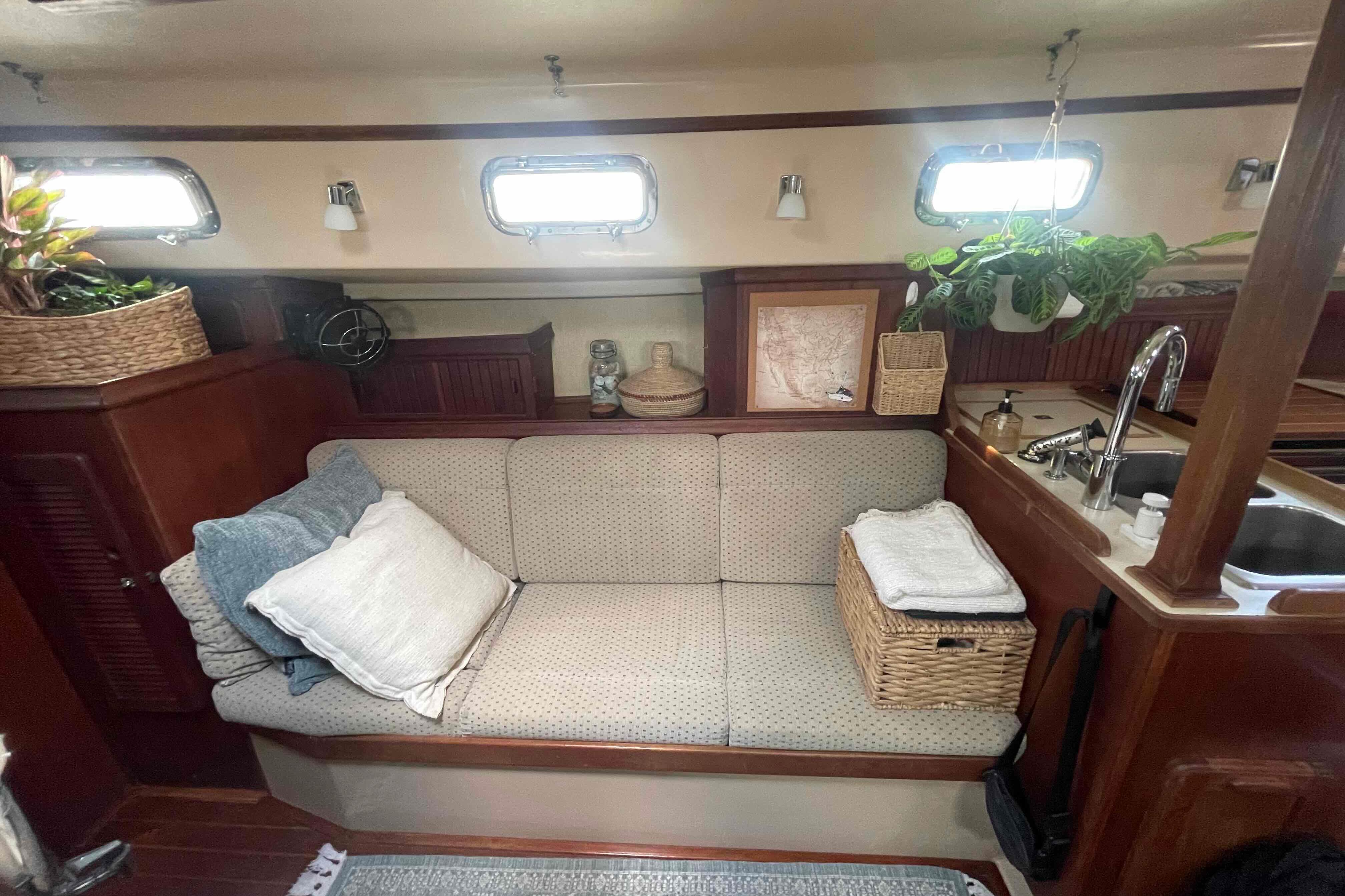 Cozy interior of 1989 Island Packet 35 sailboat with sofa, plants, and kitchen area.