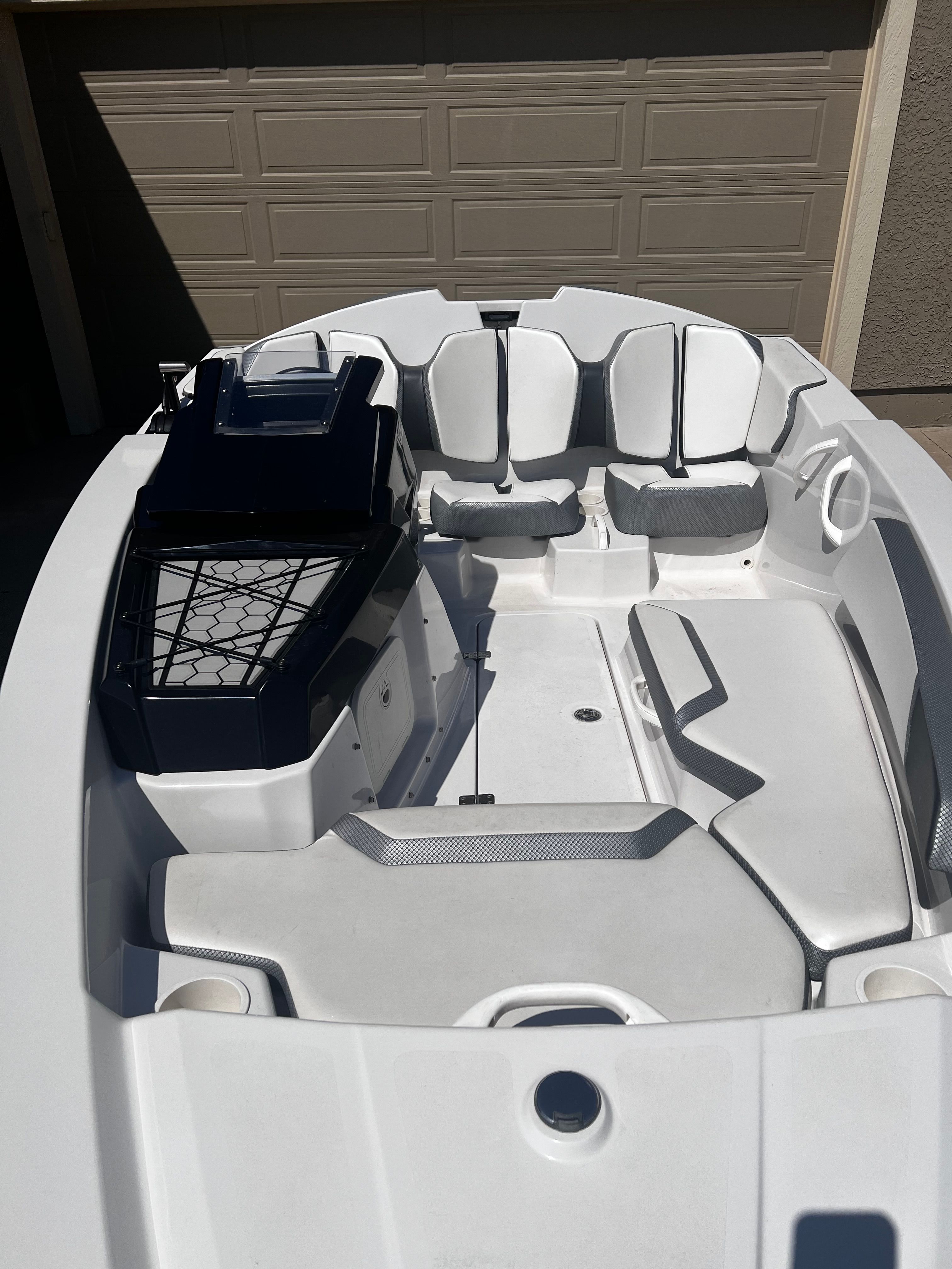 A white motorboat with gray seating is parked in a garage.