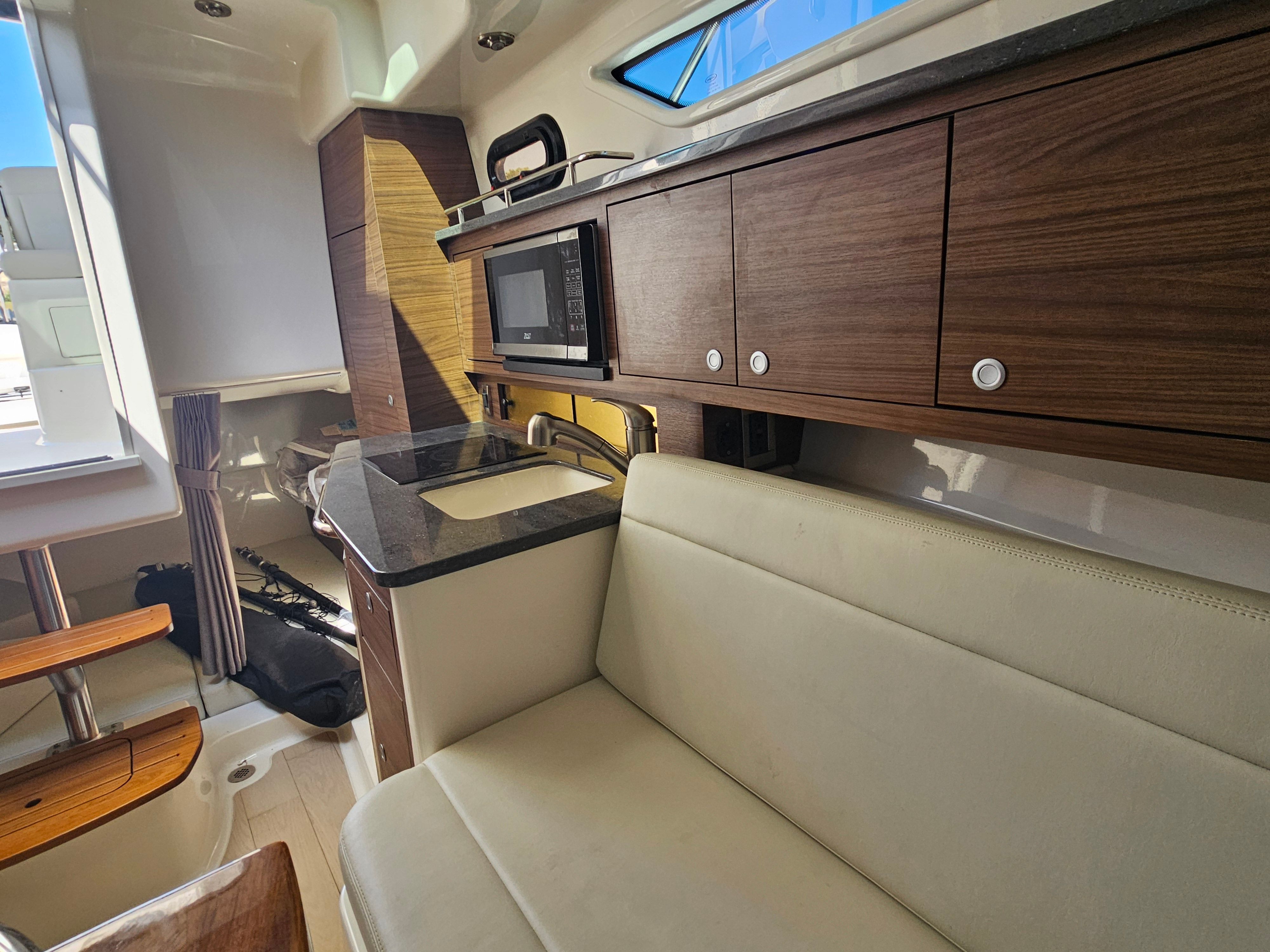 Interior of a Boston Whaler 325 Conquest with seating, wooden cabinets, and a microwave.
