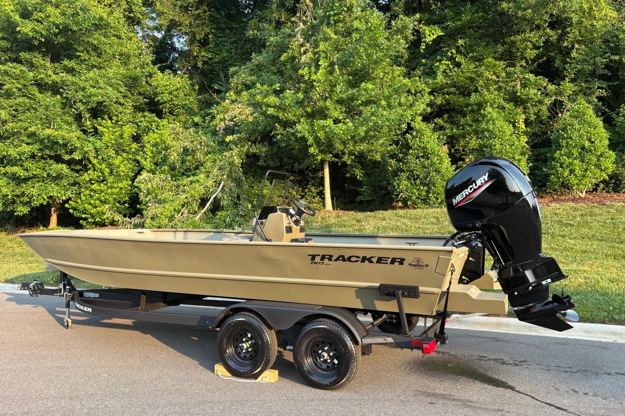 2026 Tracker Grizzly 2072 CC boat on trailer, parked near lush greenery.
