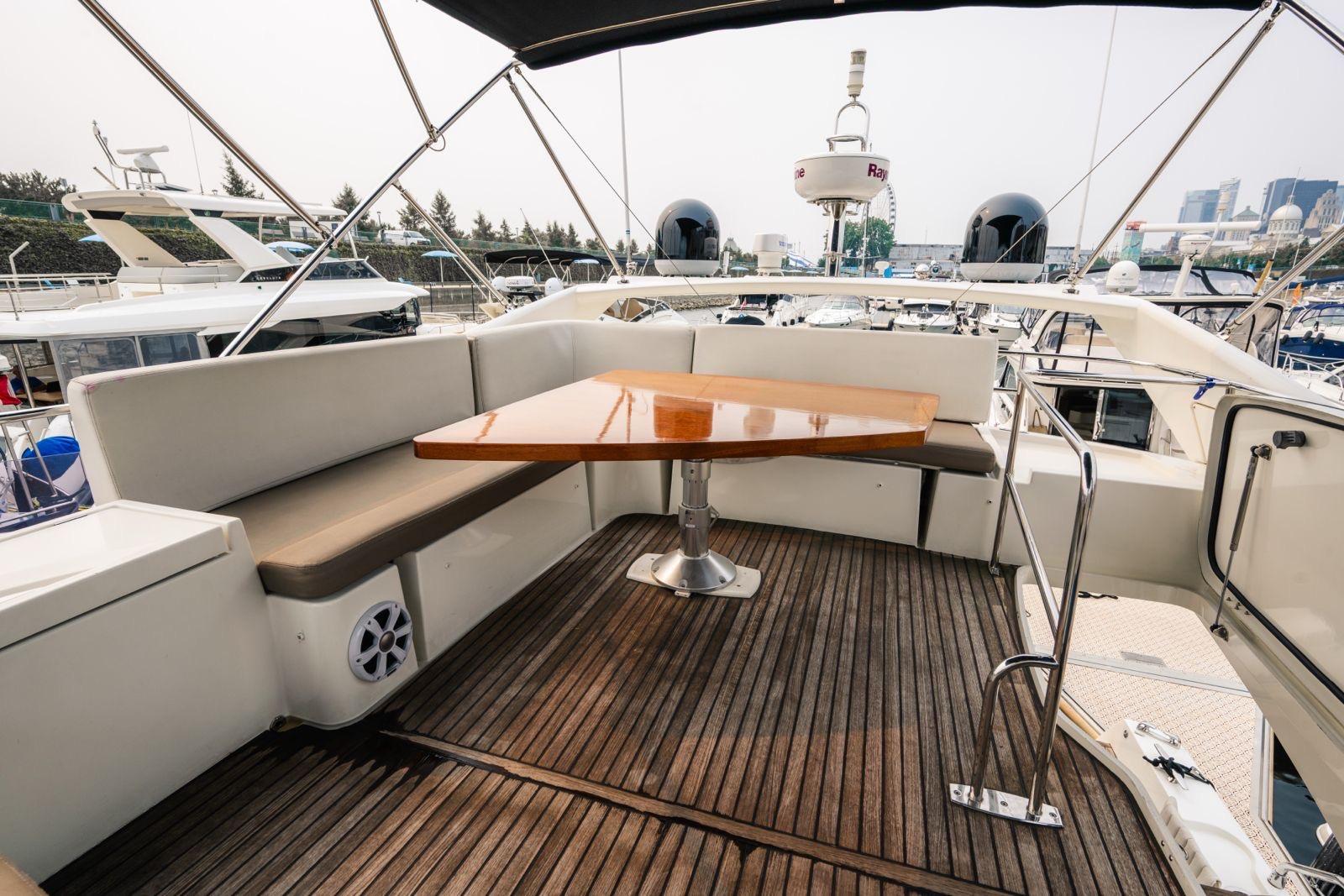 Flybridge seating area on a 2015 Prestige 500 yacht with wooden table and cushioned benches.