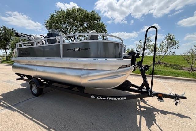 2026 Sun Tracker Bass Buggy 16 XL Select pontoon boat on trailer, parked outdoors.