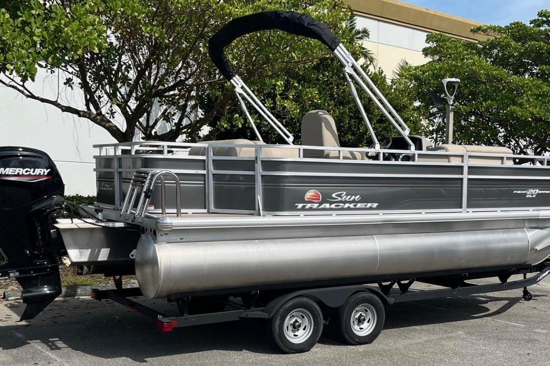 2025 Sun Tracker Fishin' Barge 20 DLX pontoon boat on trailer, parked outdoors.