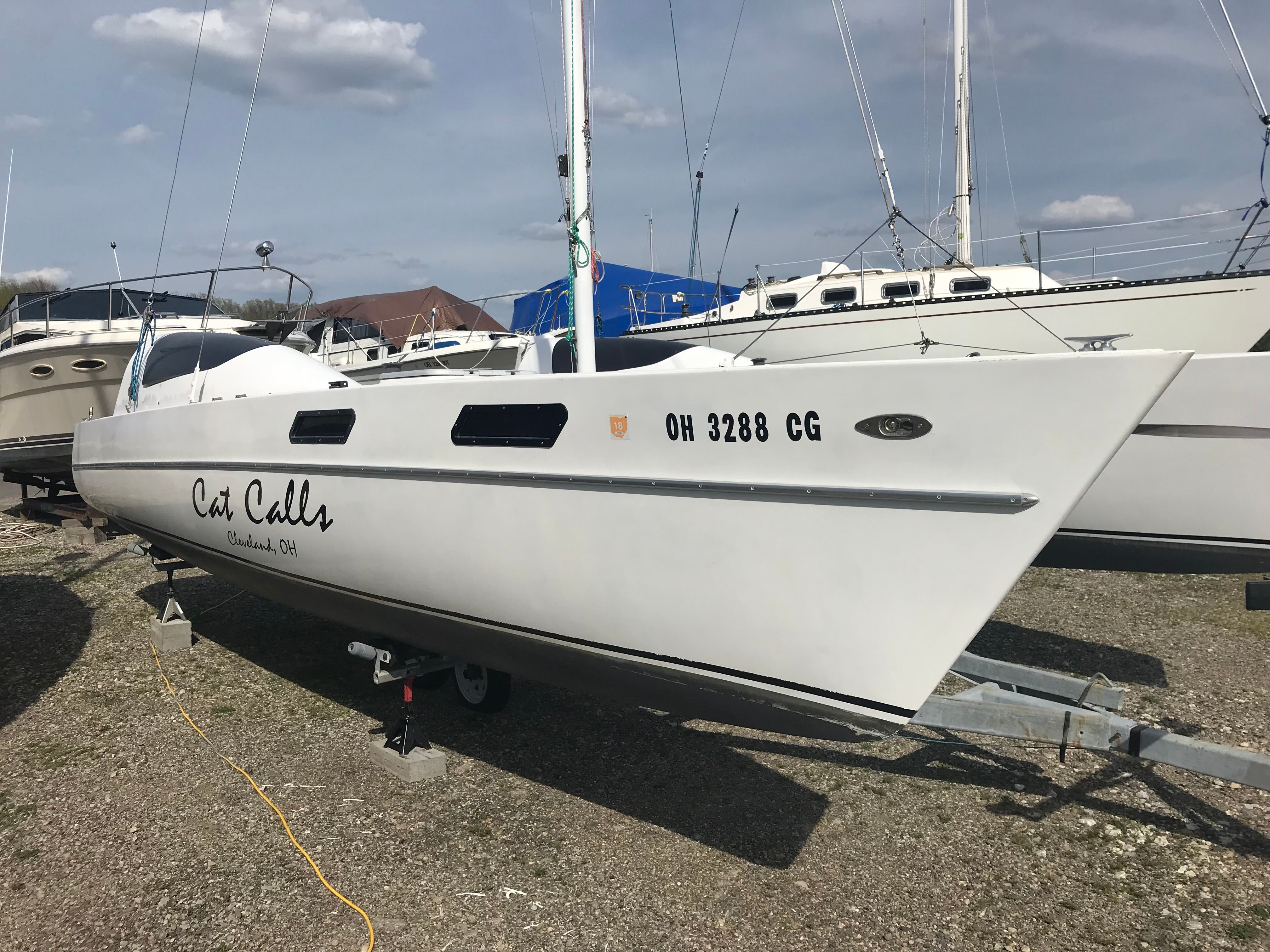A white catamaran named "Cat Calls" is on a trailer on land.