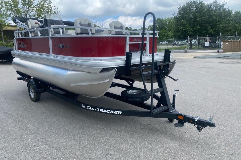 2026 Sun Tracker Bass Buggy 16 XL Select pontoon boat on trailer, parked outdoors.