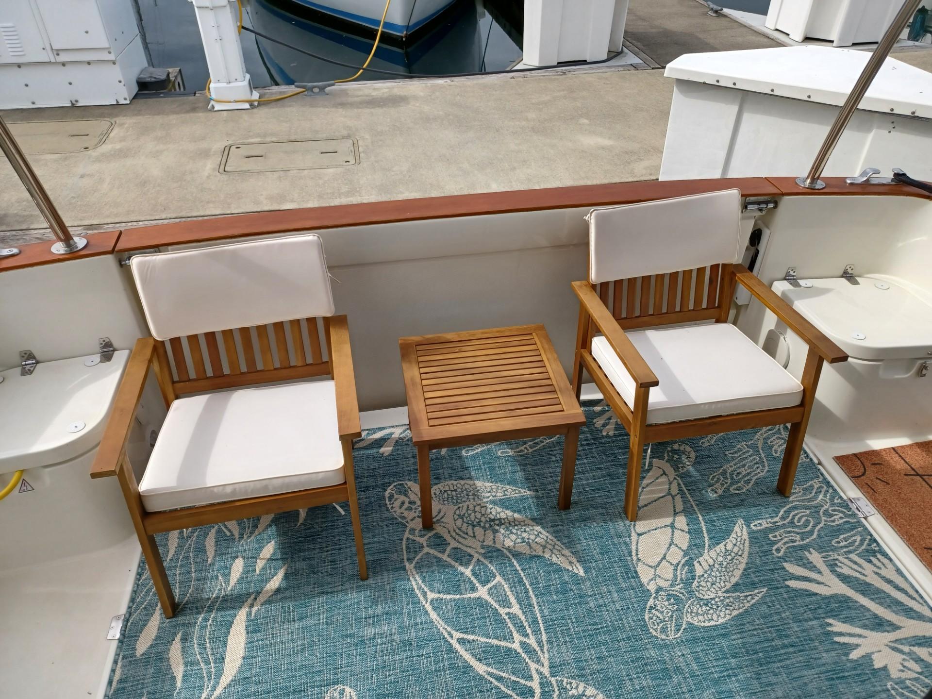 Deck of 2020 Greenline 40 yacht with wooden chairs and table on a nautical-themed rug.