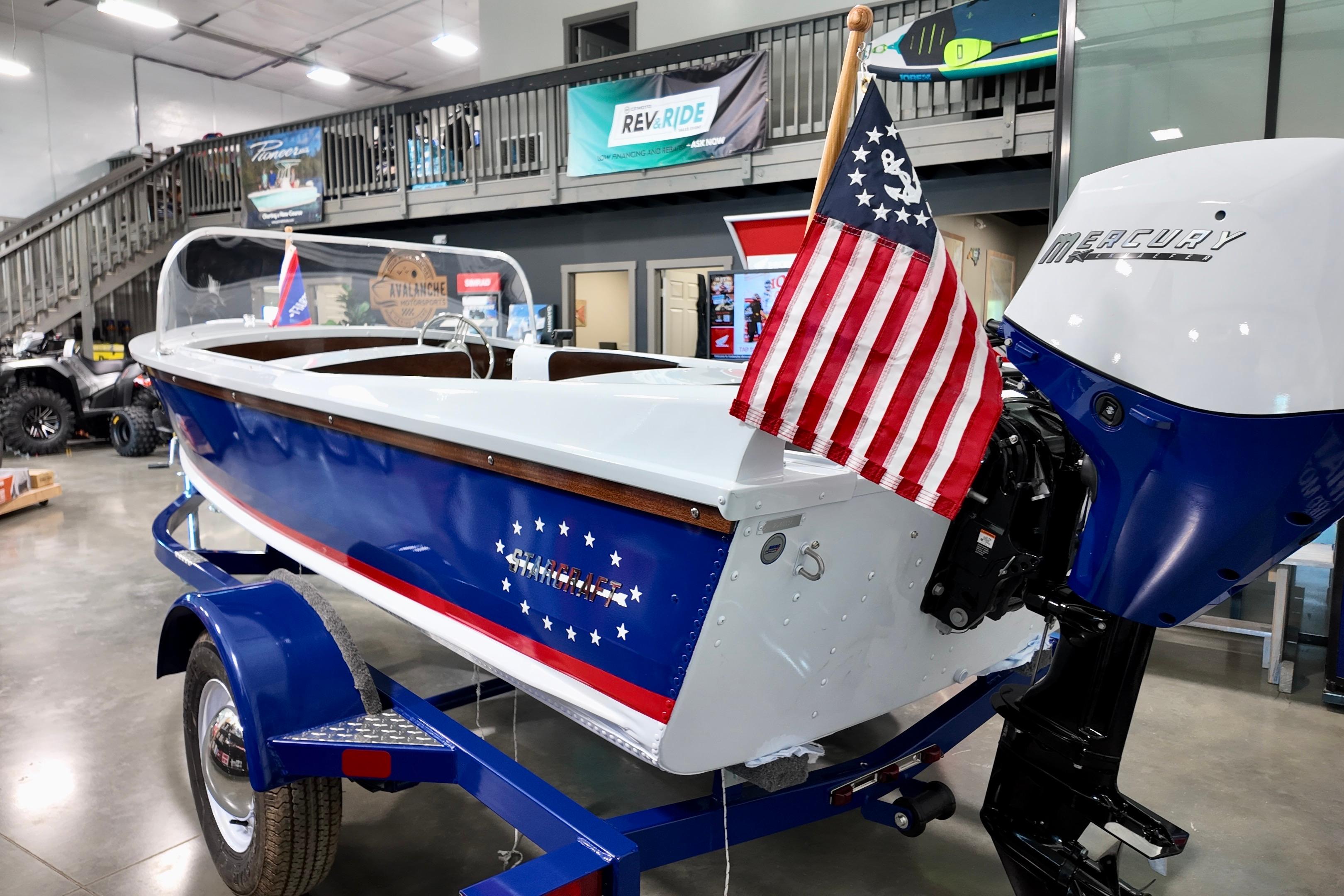 2026 Starcraft 57 Ski Champ boat with American flag, displayed indoors.