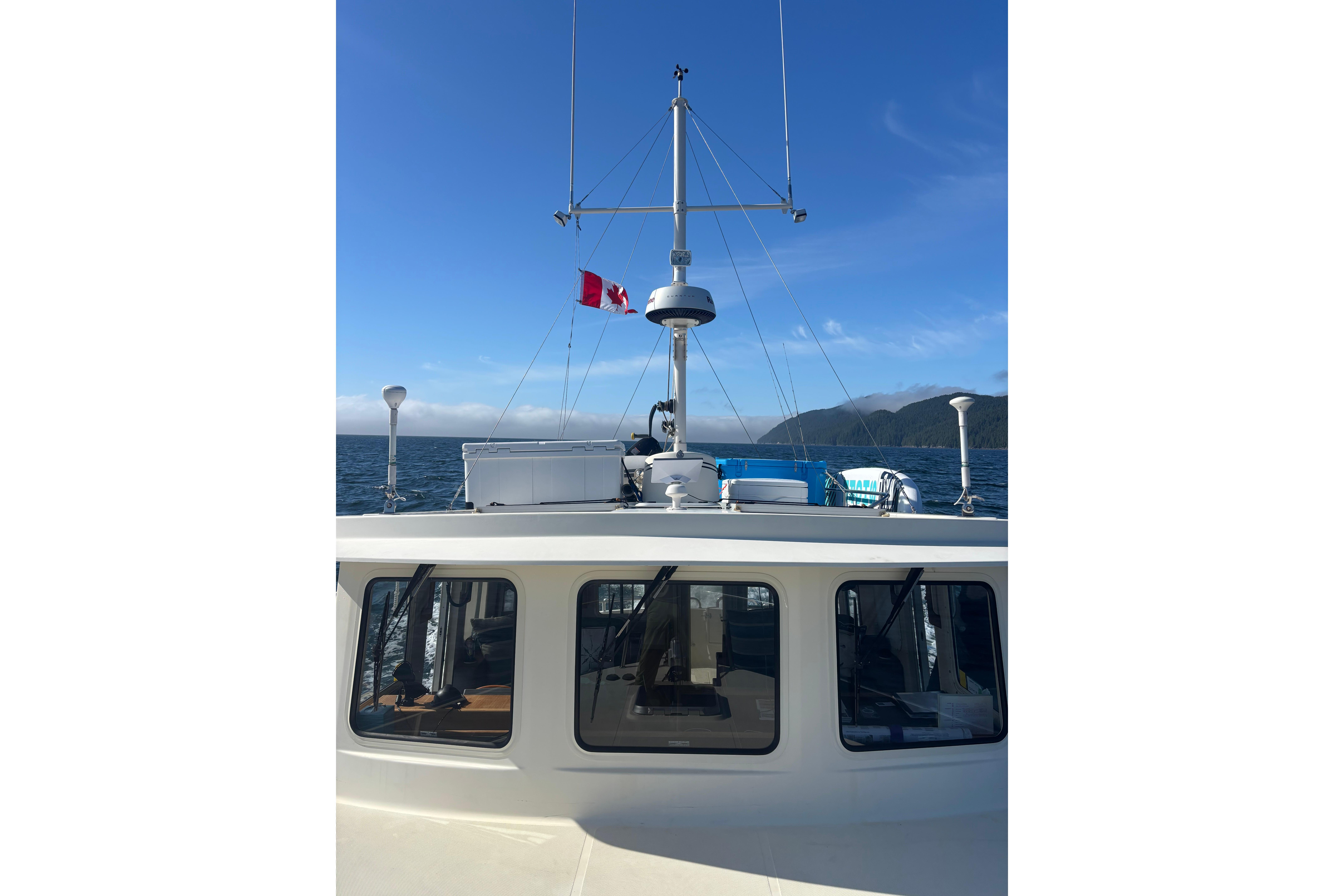 Nordic Tug 37 (2004) cruising with Canadian flag, ocean and mountains in background.