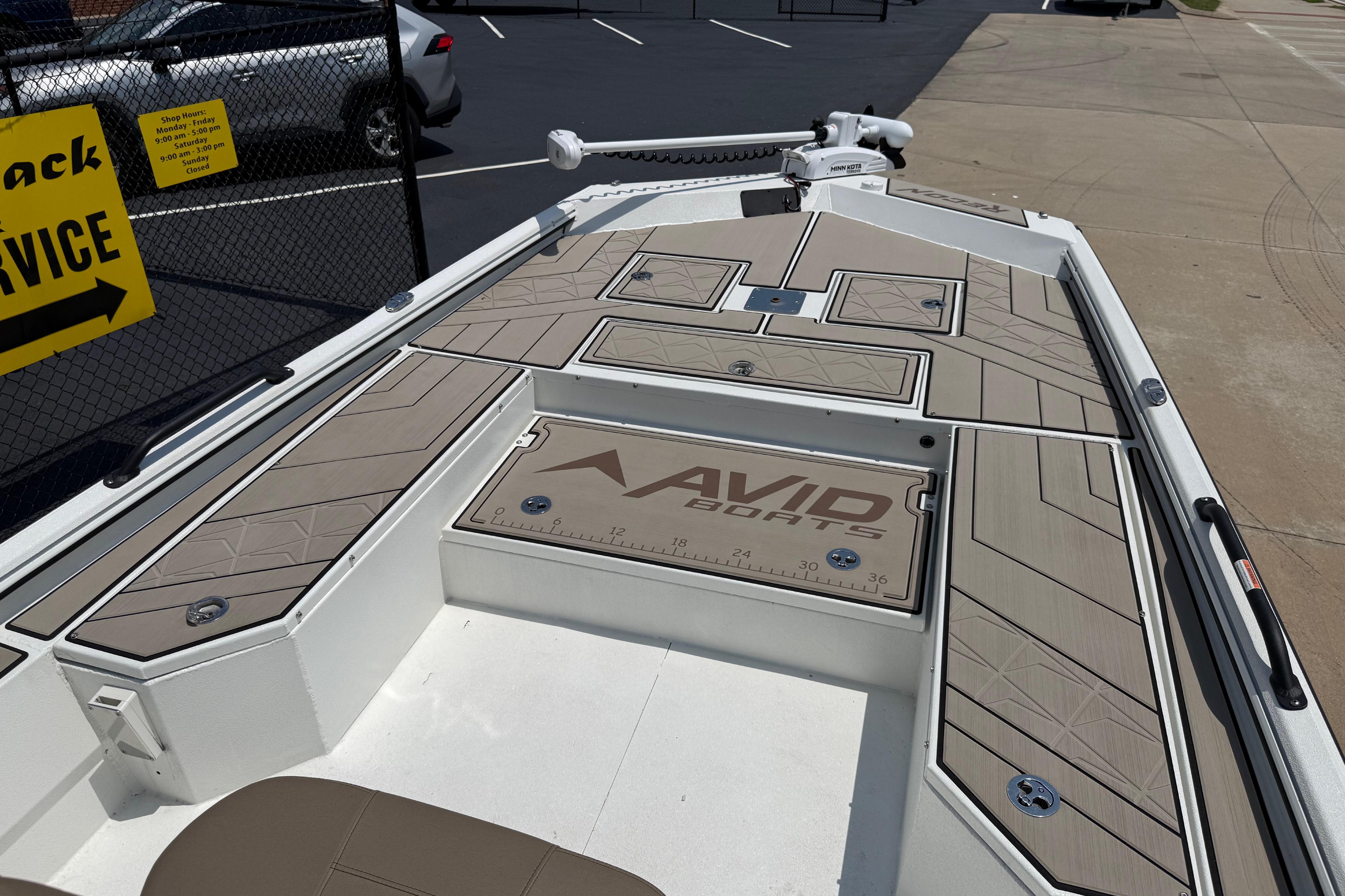 Avid 22 Recon 2025 boat deck with storage compartments and logo in a parking lot.