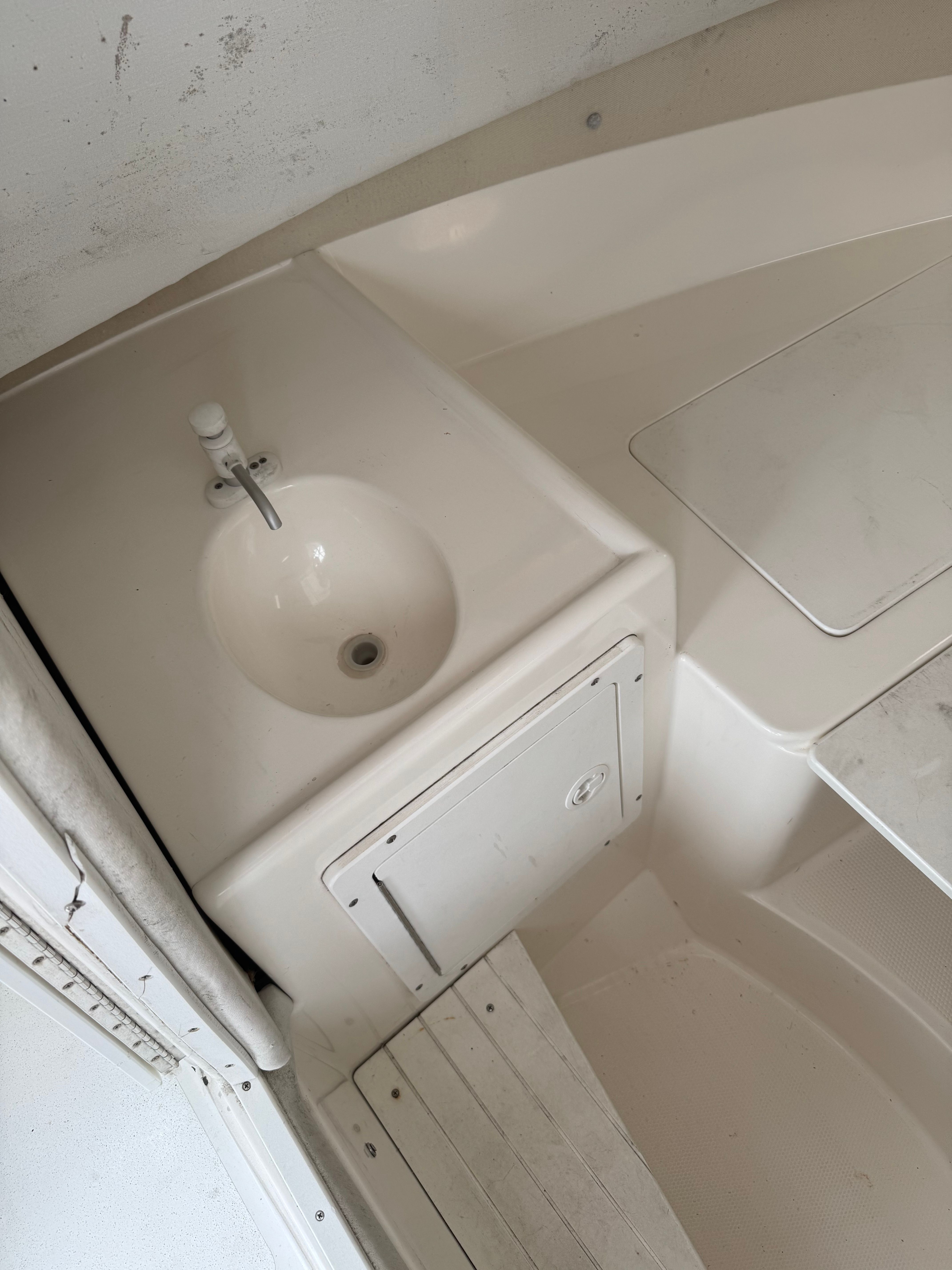 The image shows a sink on a boat, surrounded by white surfaces and a small storage area.