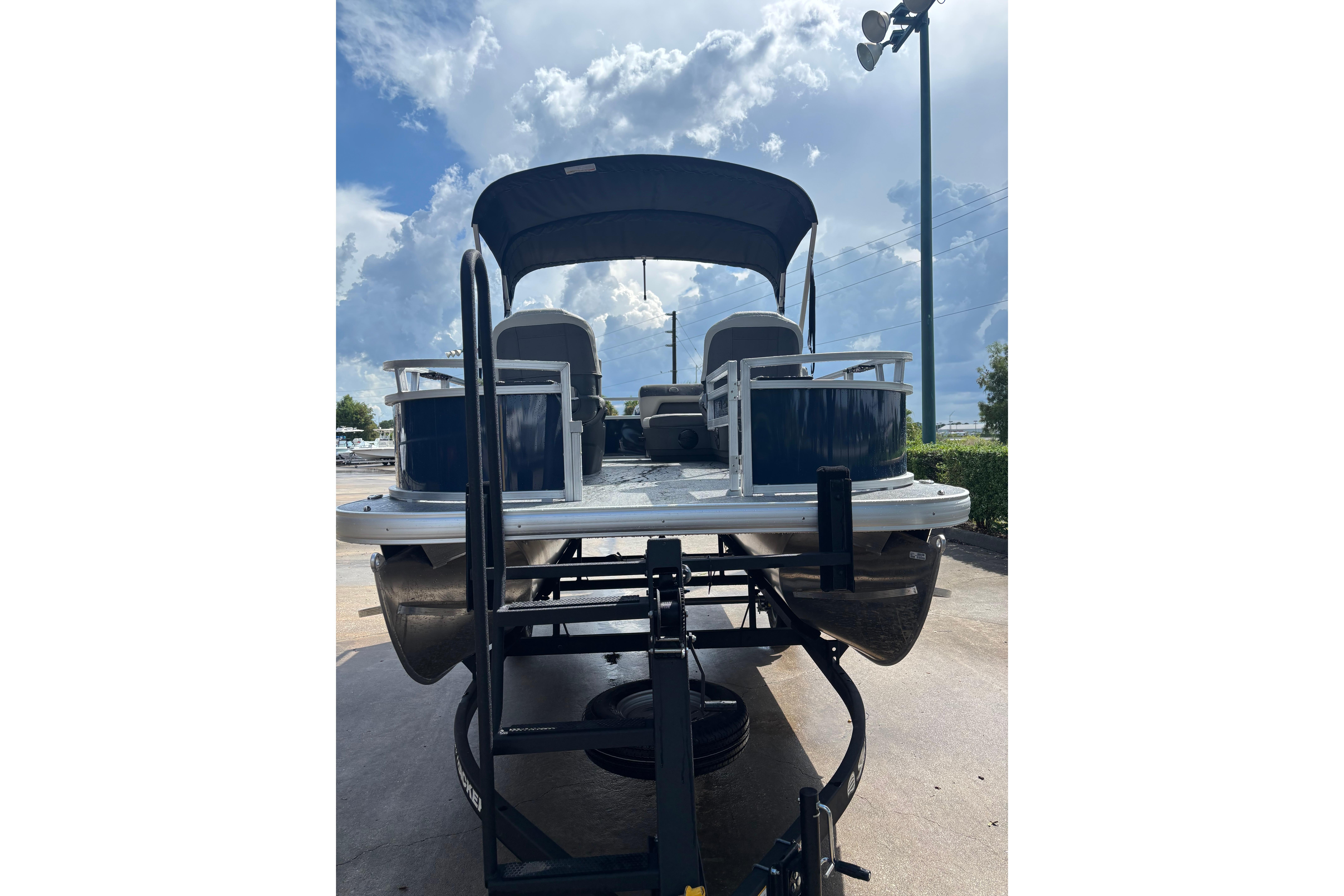2026 Sun Tracker Bass Buggy 16 XL Select pontoon boat on trailer under cloudy sky.
