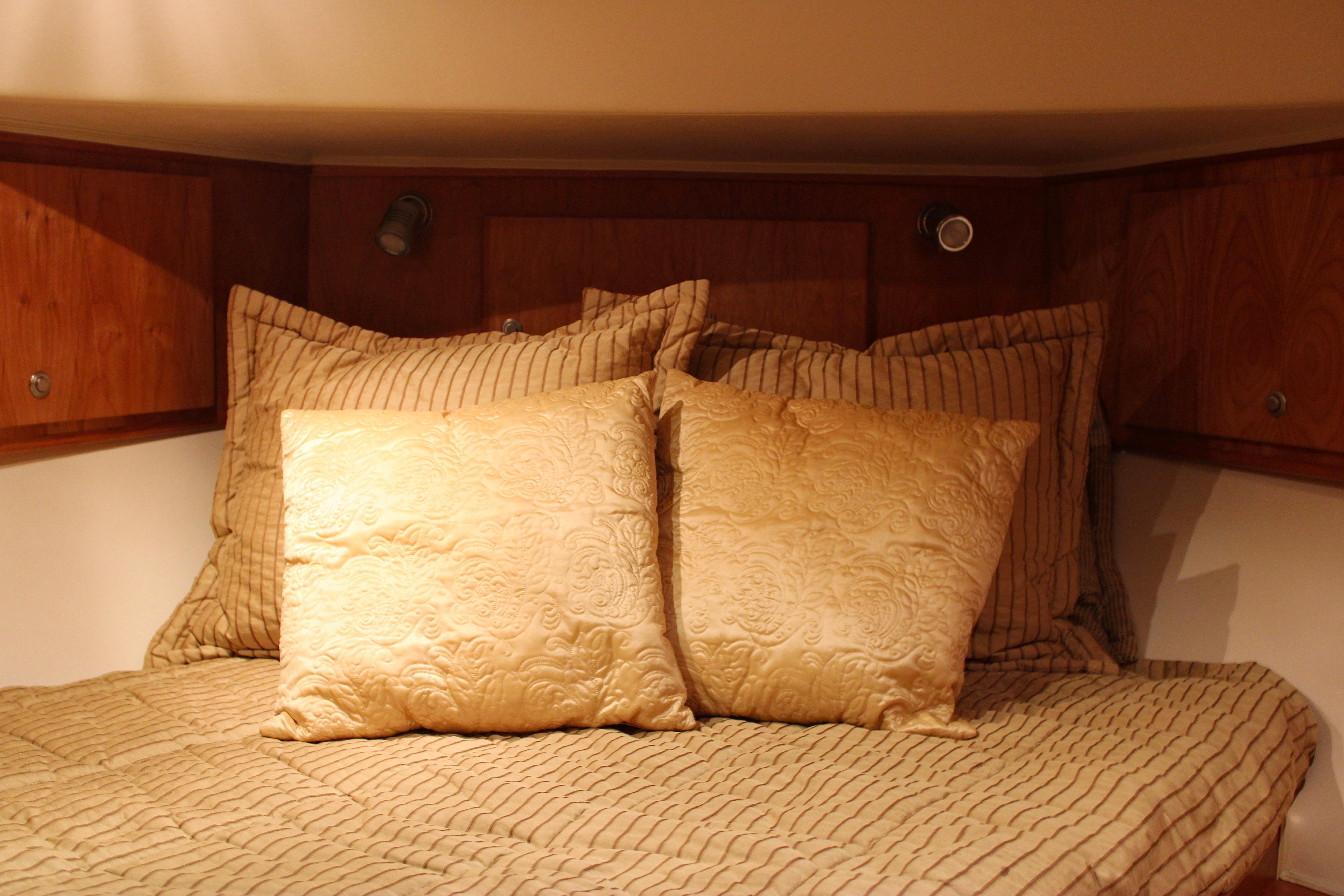Luxurious bedding in a 2007 Navigator 5100 yacht cabin with elegant pillows and wood paneling.