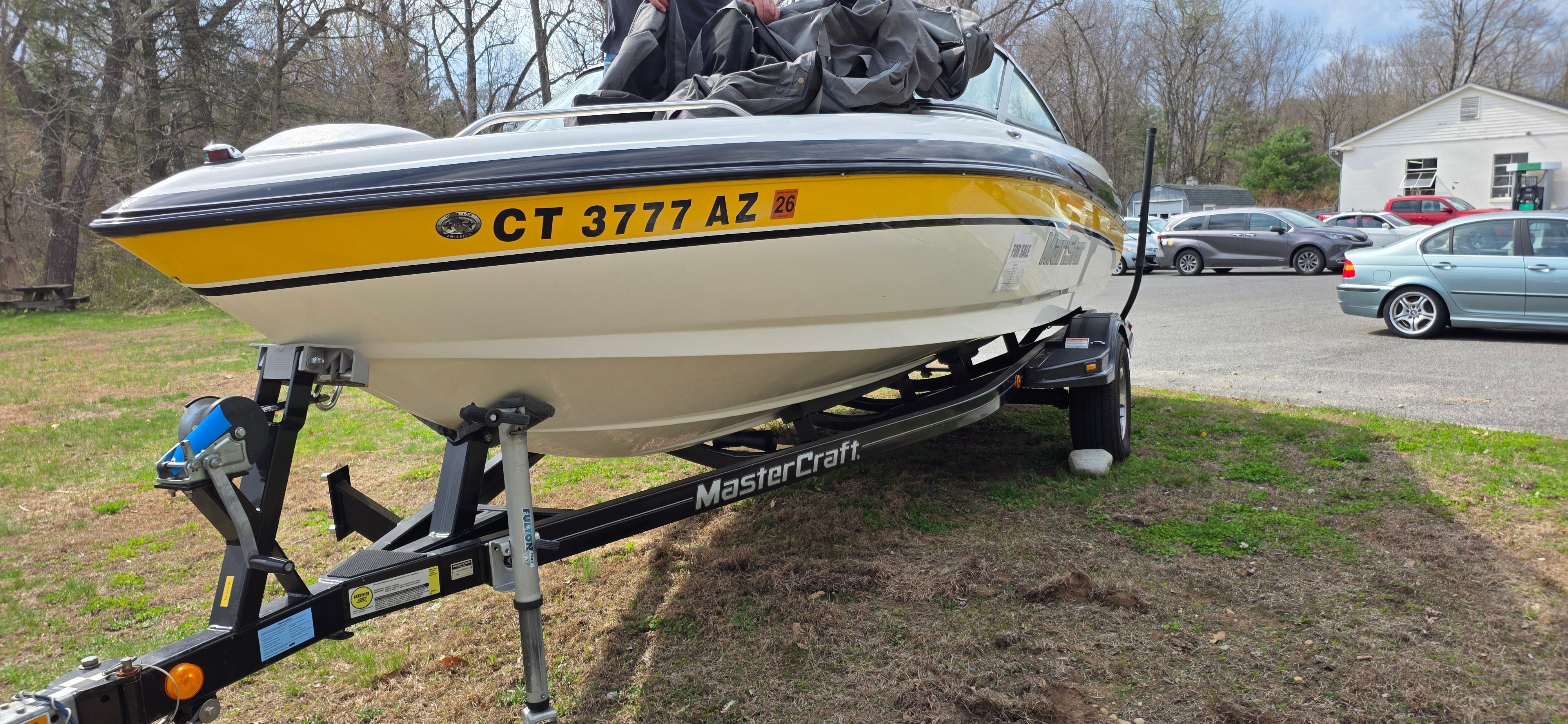 2004 MasterCraft Maristar boat on trailer, yellow and white, parked outdoors.
