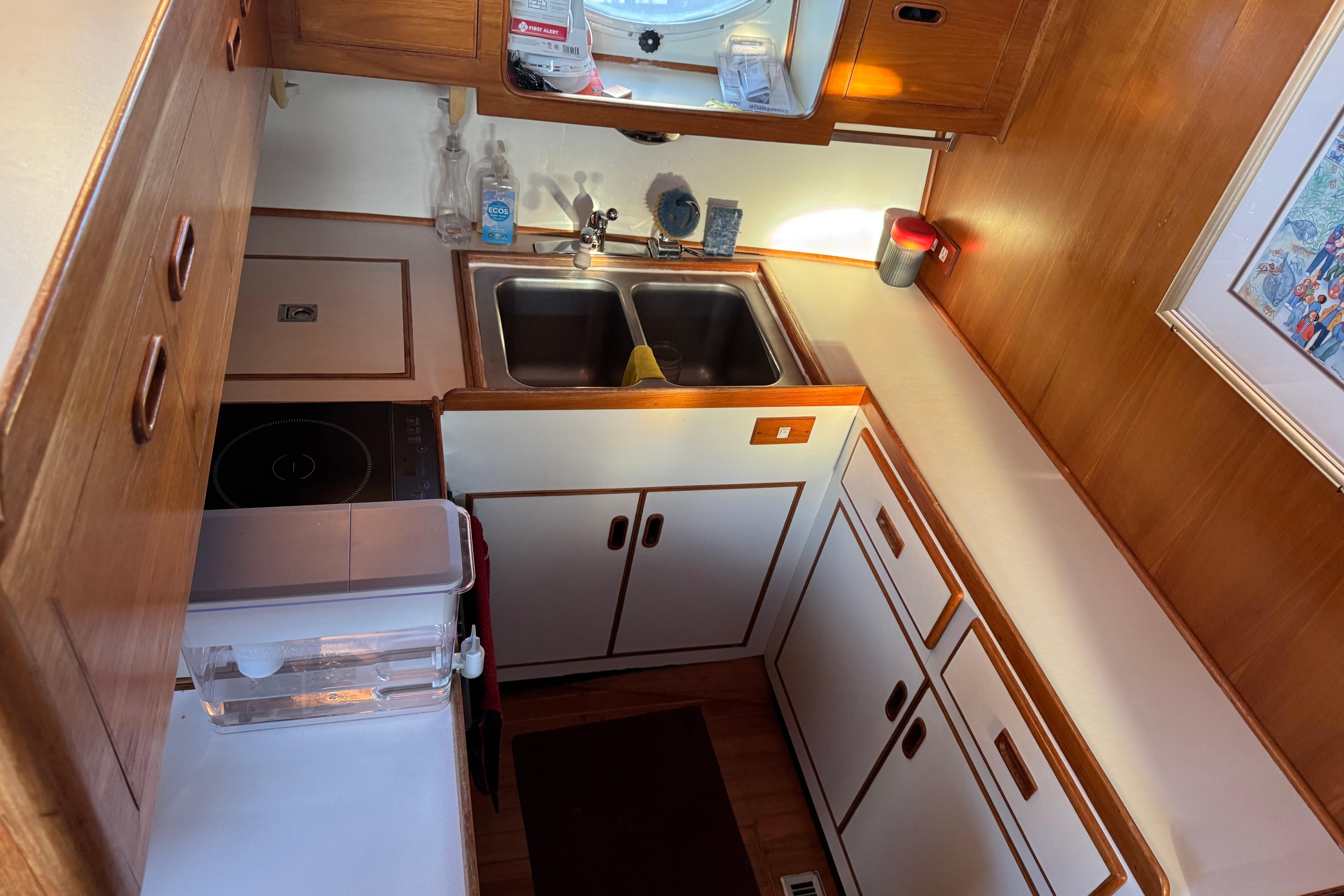 Compact kitchen in a 1987 President 37 boat with wooden cabinetry and dual sinks.