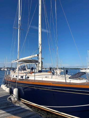 An elegant sailboat with a blue hull docked at a sunny pier.