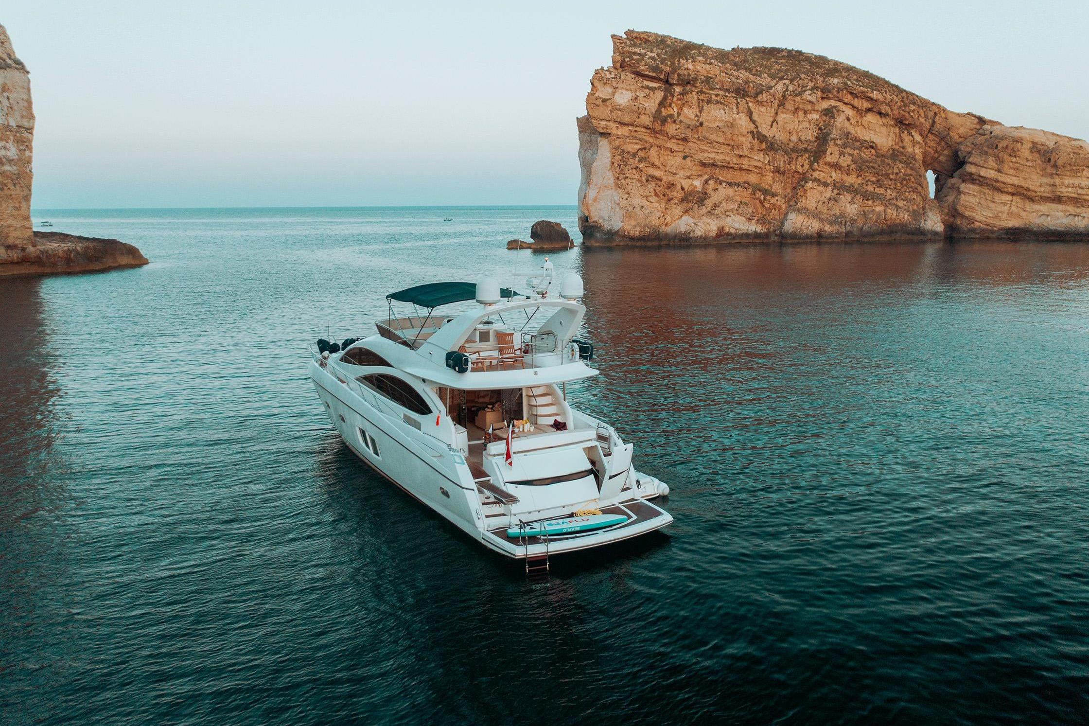 Luxury Sunseeker Manhattan 70 yacht, 2008 model, anchored near rocky coastal cliffs.