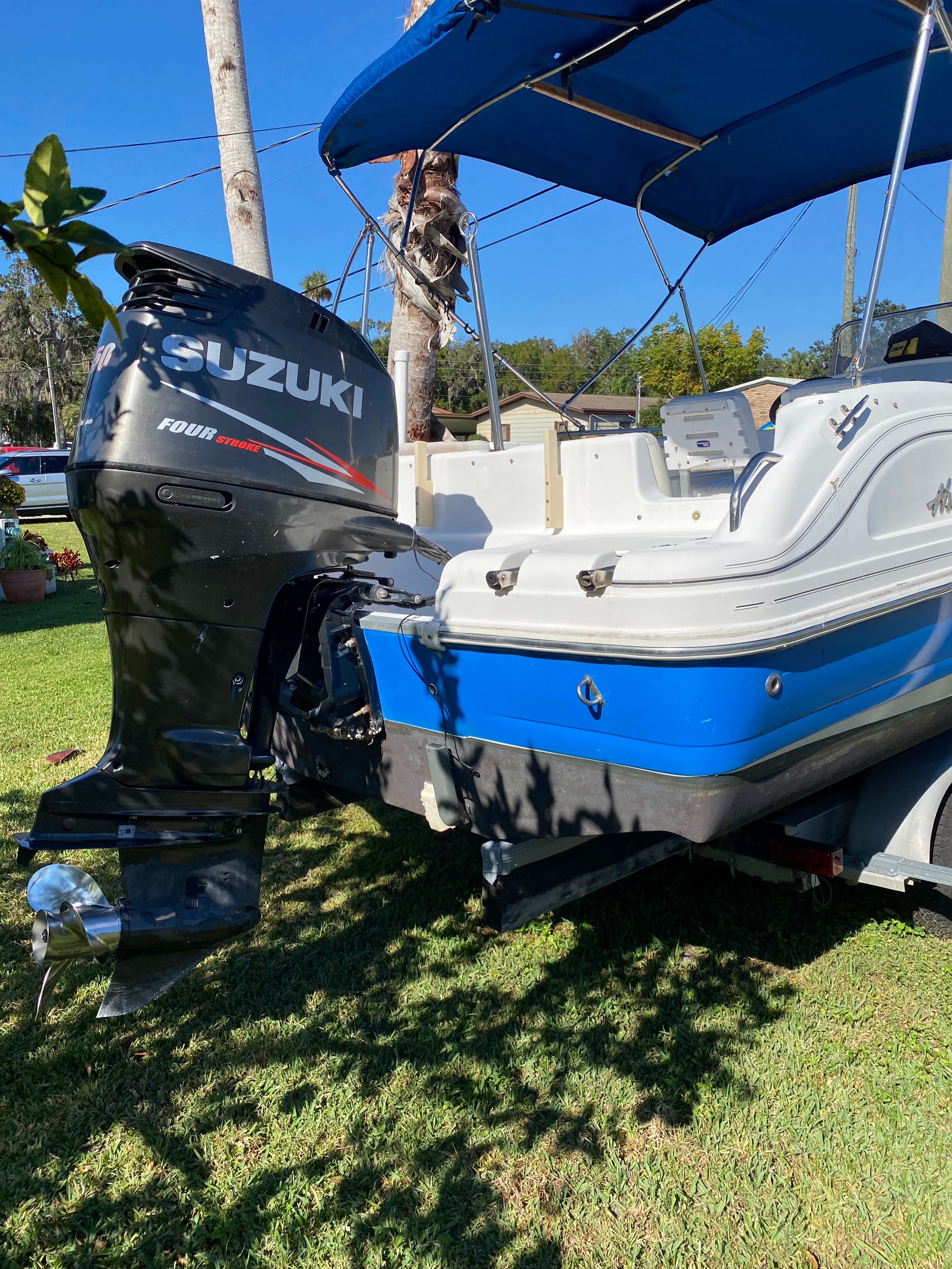 A blue and white 2012 Hurricane SunDeck Sport 231 OB with a Suzuki outboard motor on a trailer.