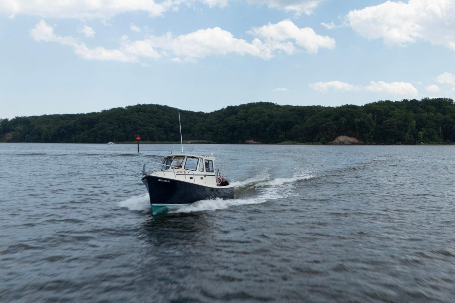 2006 Atlas Boat Works Acadia 25 cruising on a scenic lake with forested shoreline.
