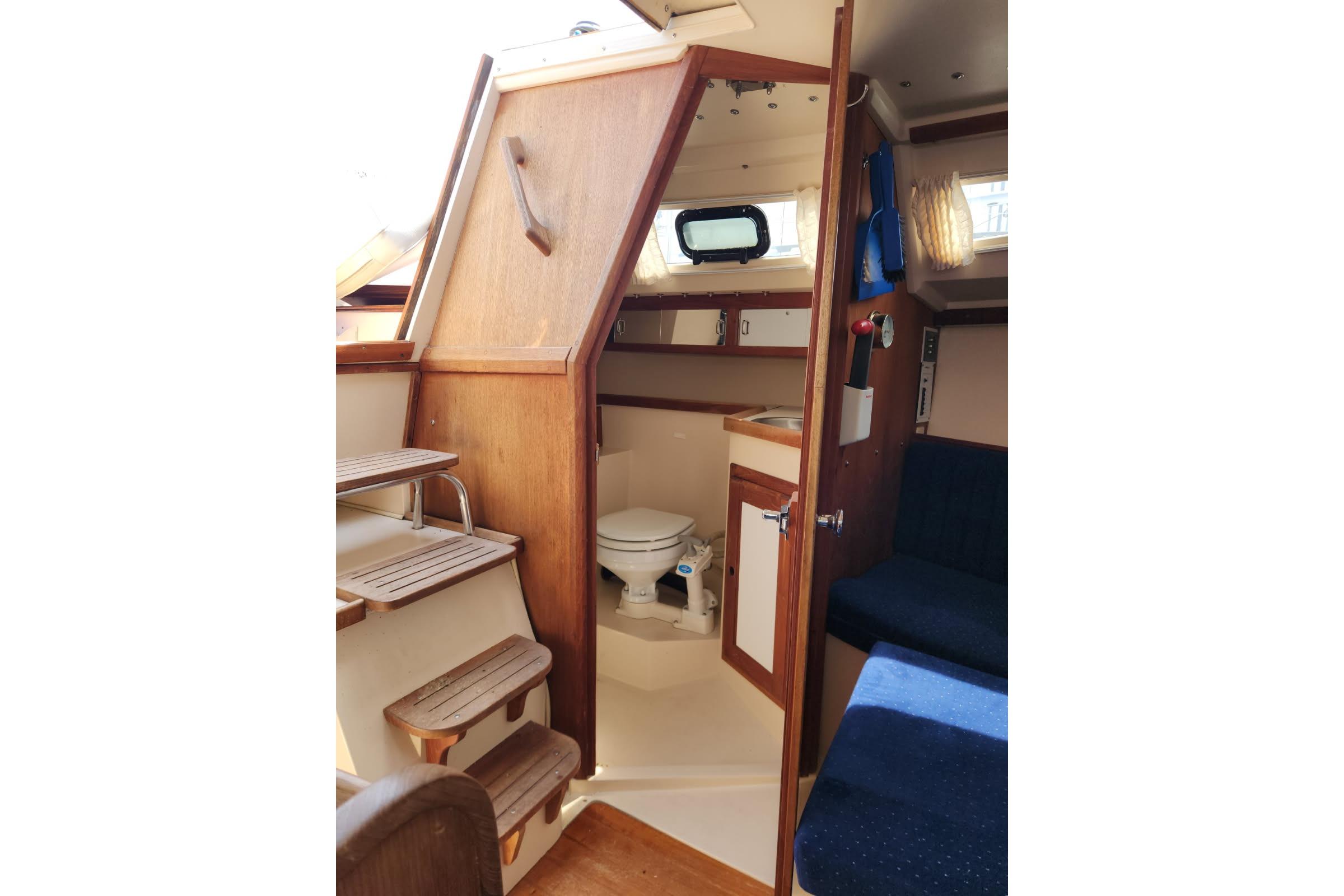 Interior of a 1990 Catalina Capri sailboat featuring a compact bathroom and wooden steps.