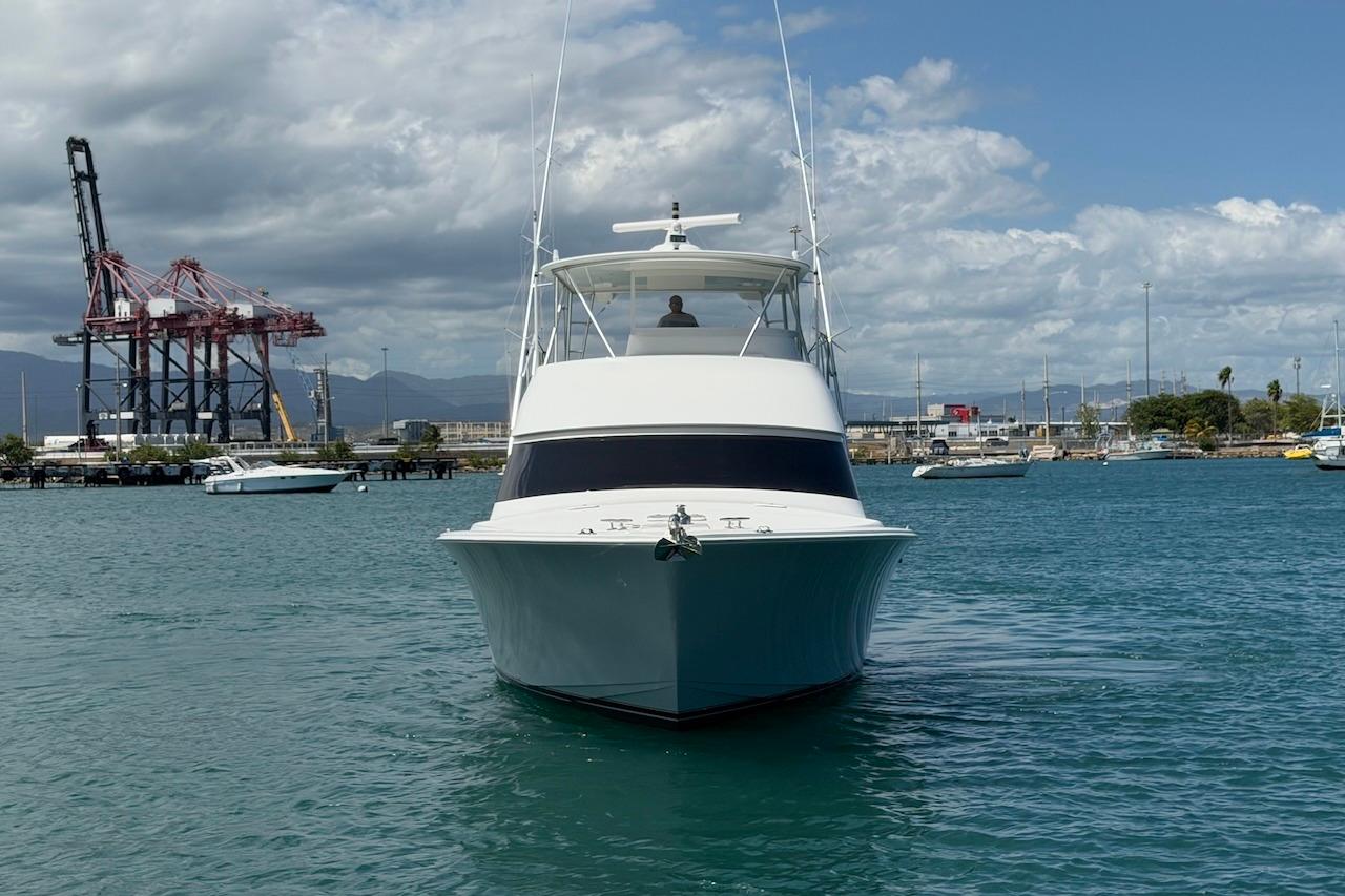 2012 Viking 50 Convertible yacht in harbor, with industrial cranes and cloudy sky backdrop.