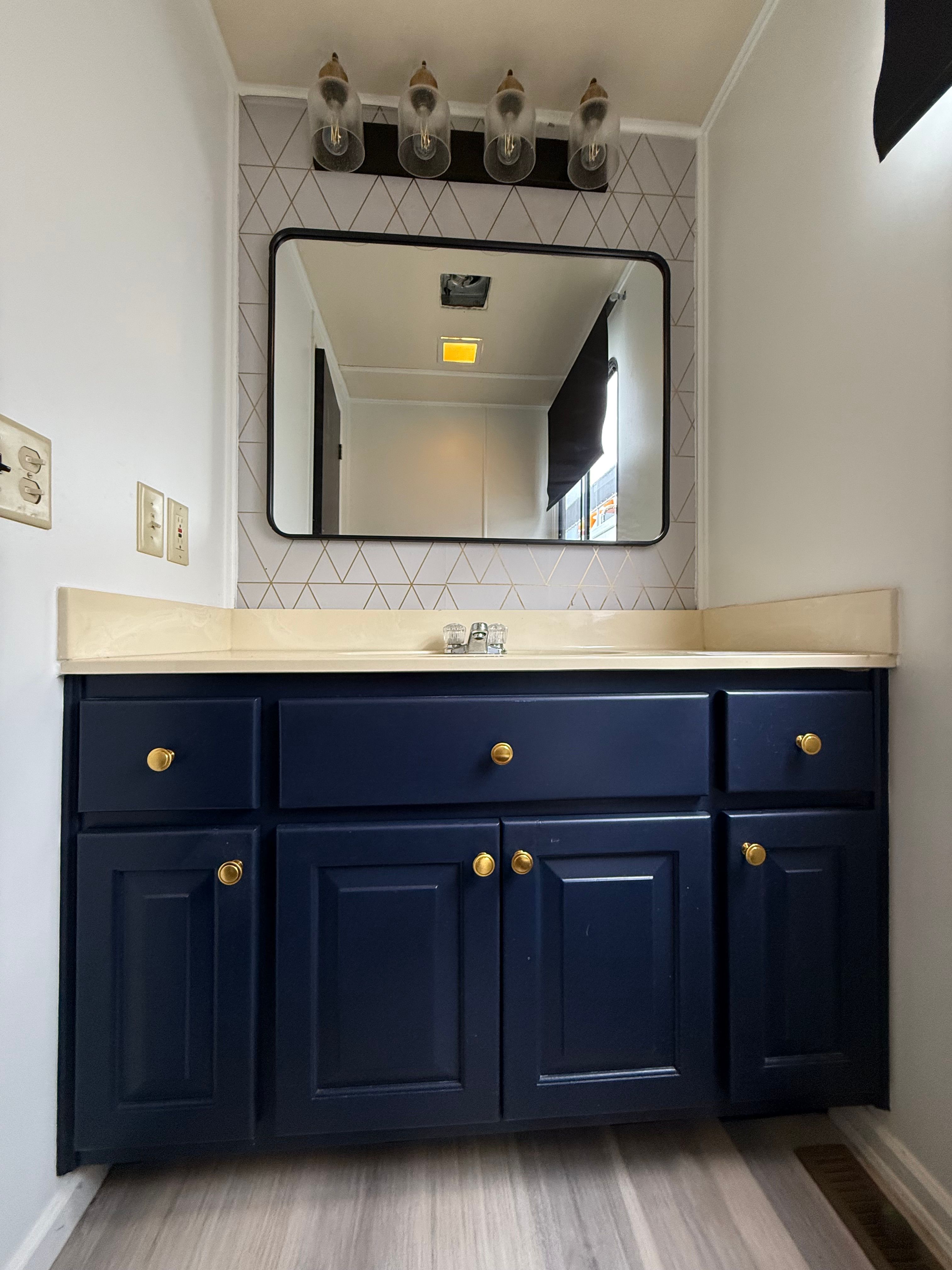 A bathroom with blue cabinets, a large mirror, and modern lighting.