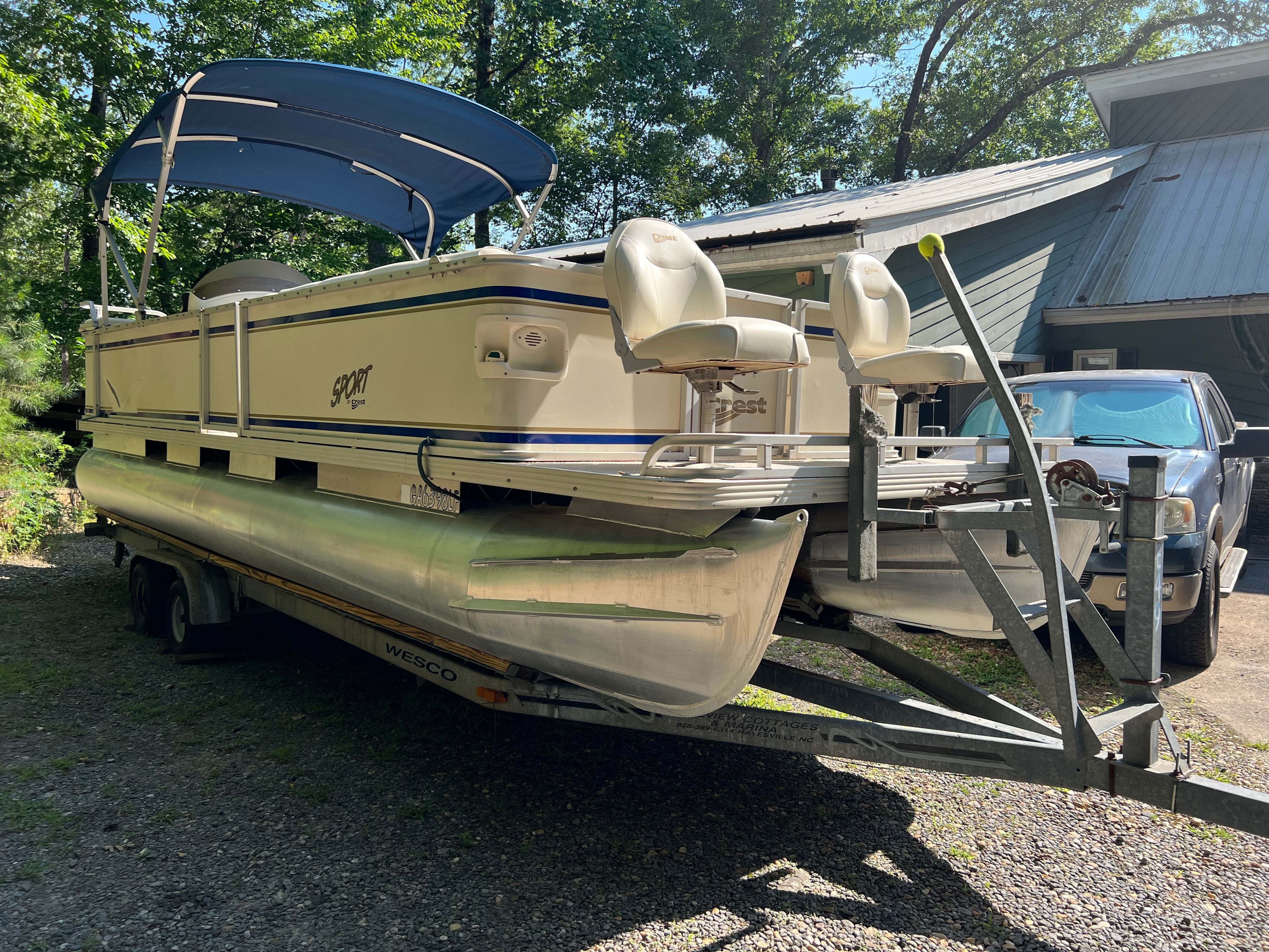 A 2003 Crest 24’ Sport pontoon boat on a trailer, featuring a blue canopy and two seats.