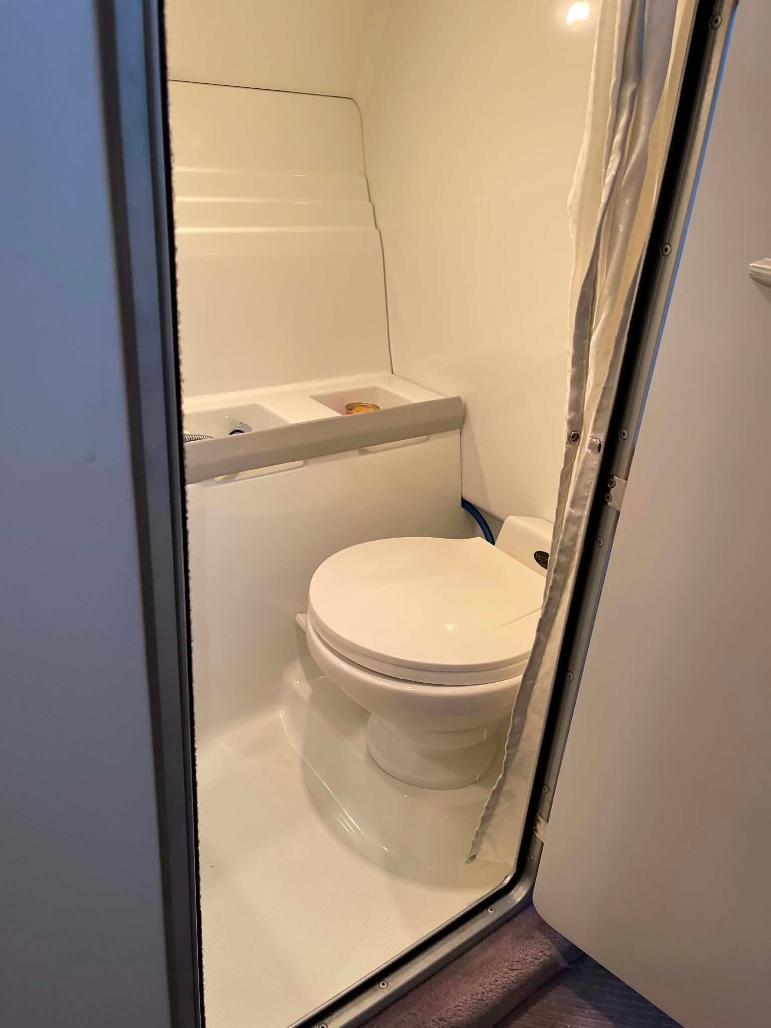 The image shows a boat toilet with white interior and a shower curtain.
