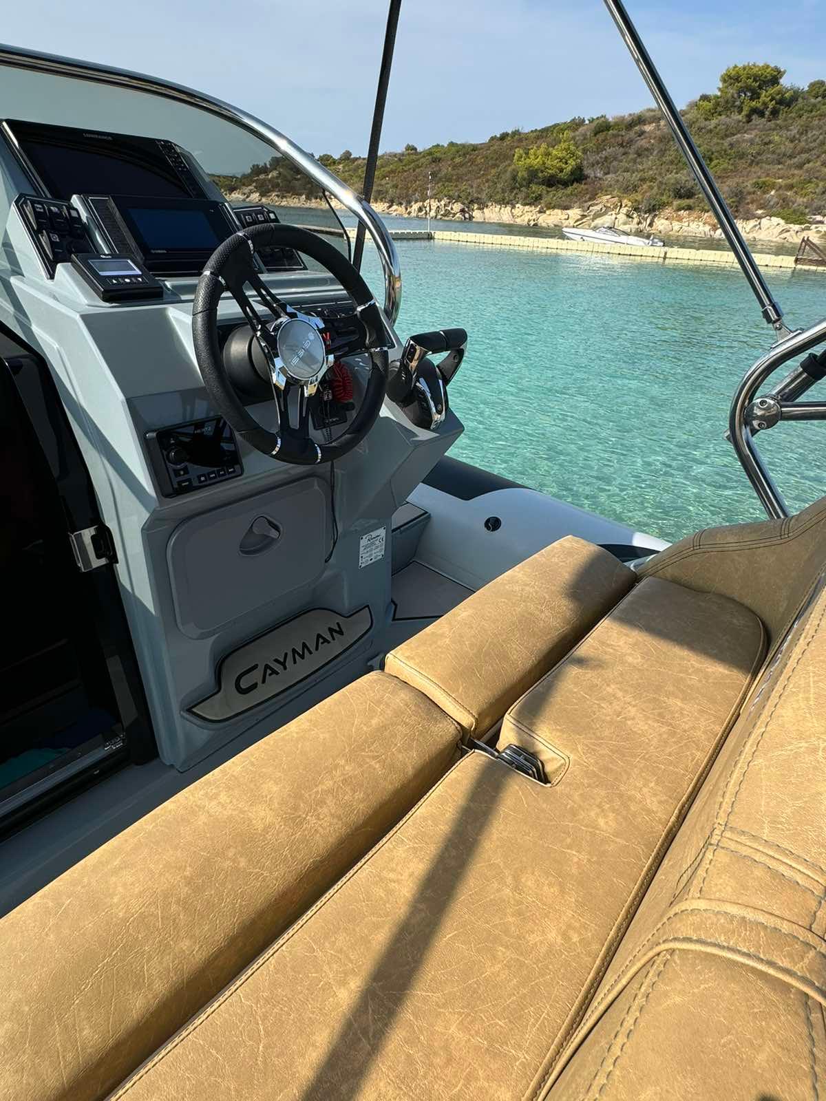 2022 Ranieri Cayman 28 Executive Trofeo boat interior with steering wheel, tan seating, and clear blue water.