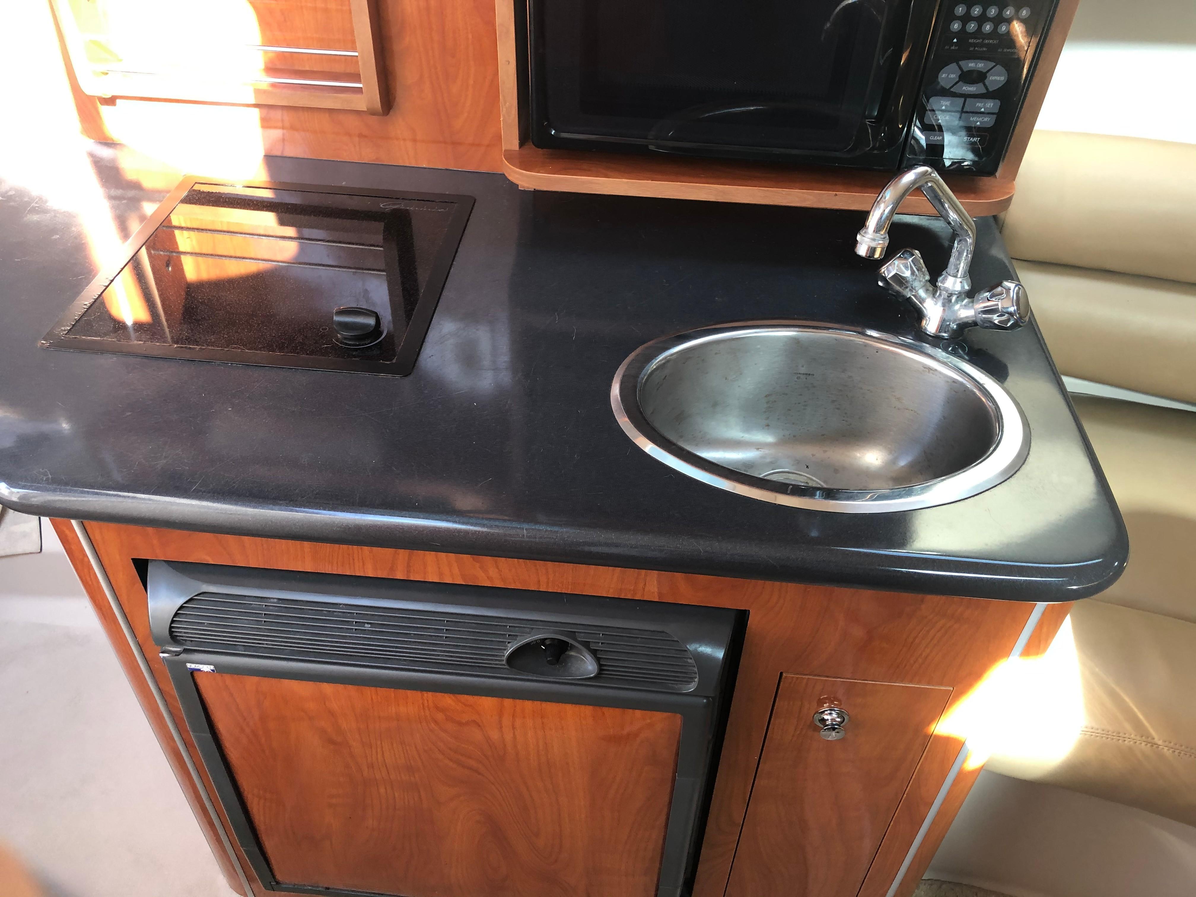 Compact kitchen area in a 2005 Doral Monticello boat with sink, stove, and microwave.