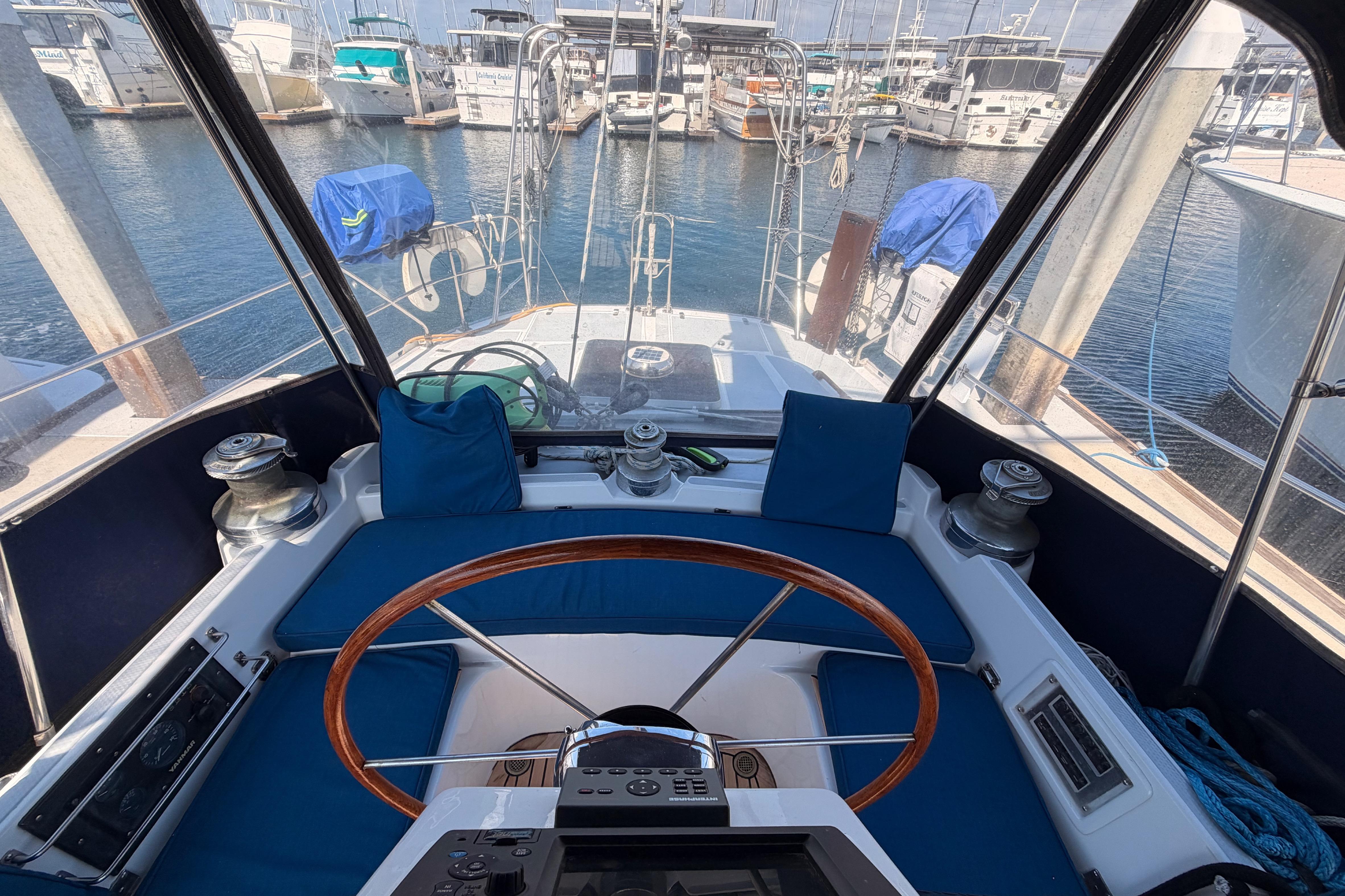 Cockpit view of a 1991 Hylas 51 sailboat, featuring a wooden steering wheel and marina backdrop.