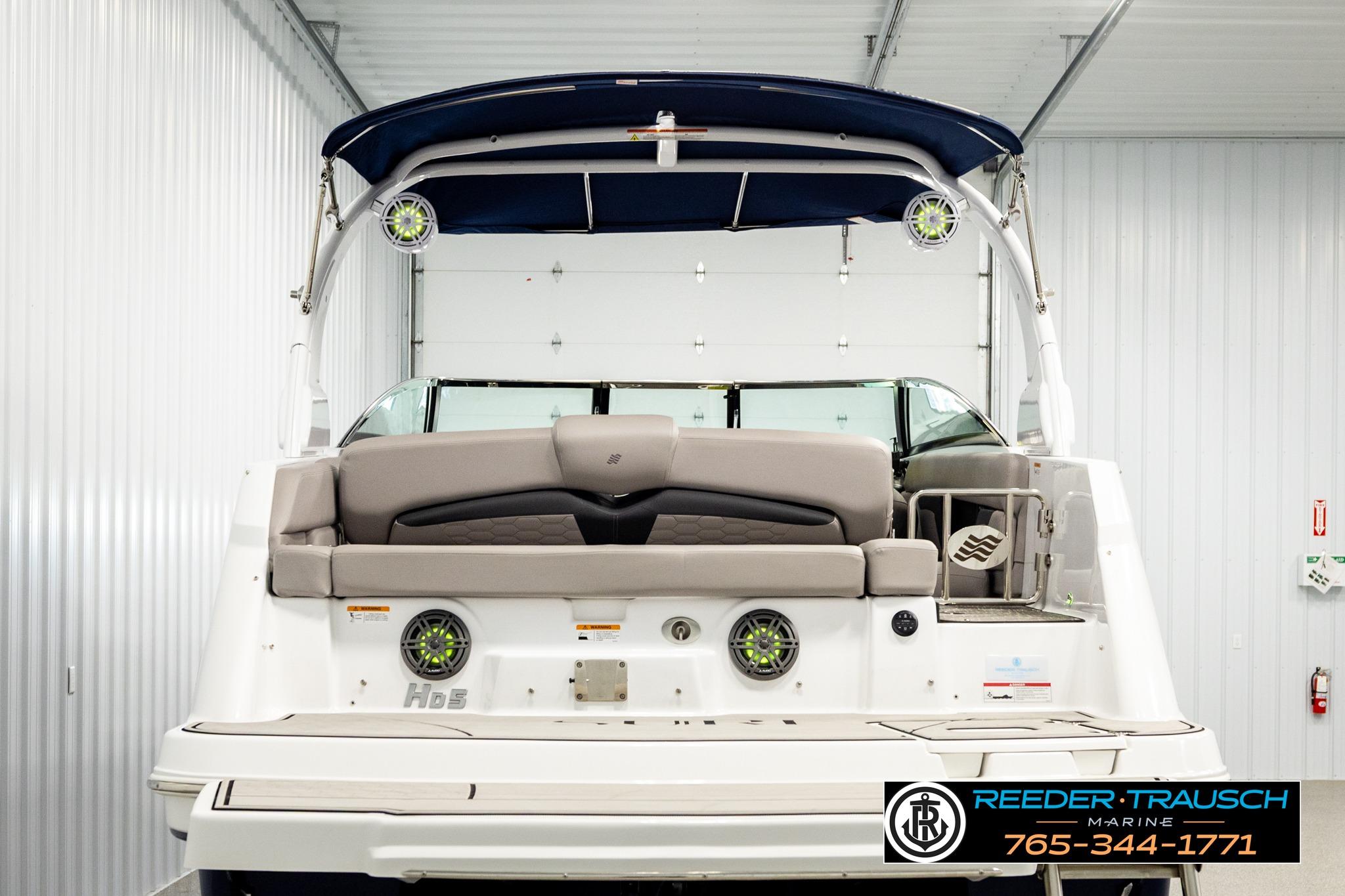 2024 FOURWINNS HD5 Surf boat in a showroom, rear view with seating and speakers.