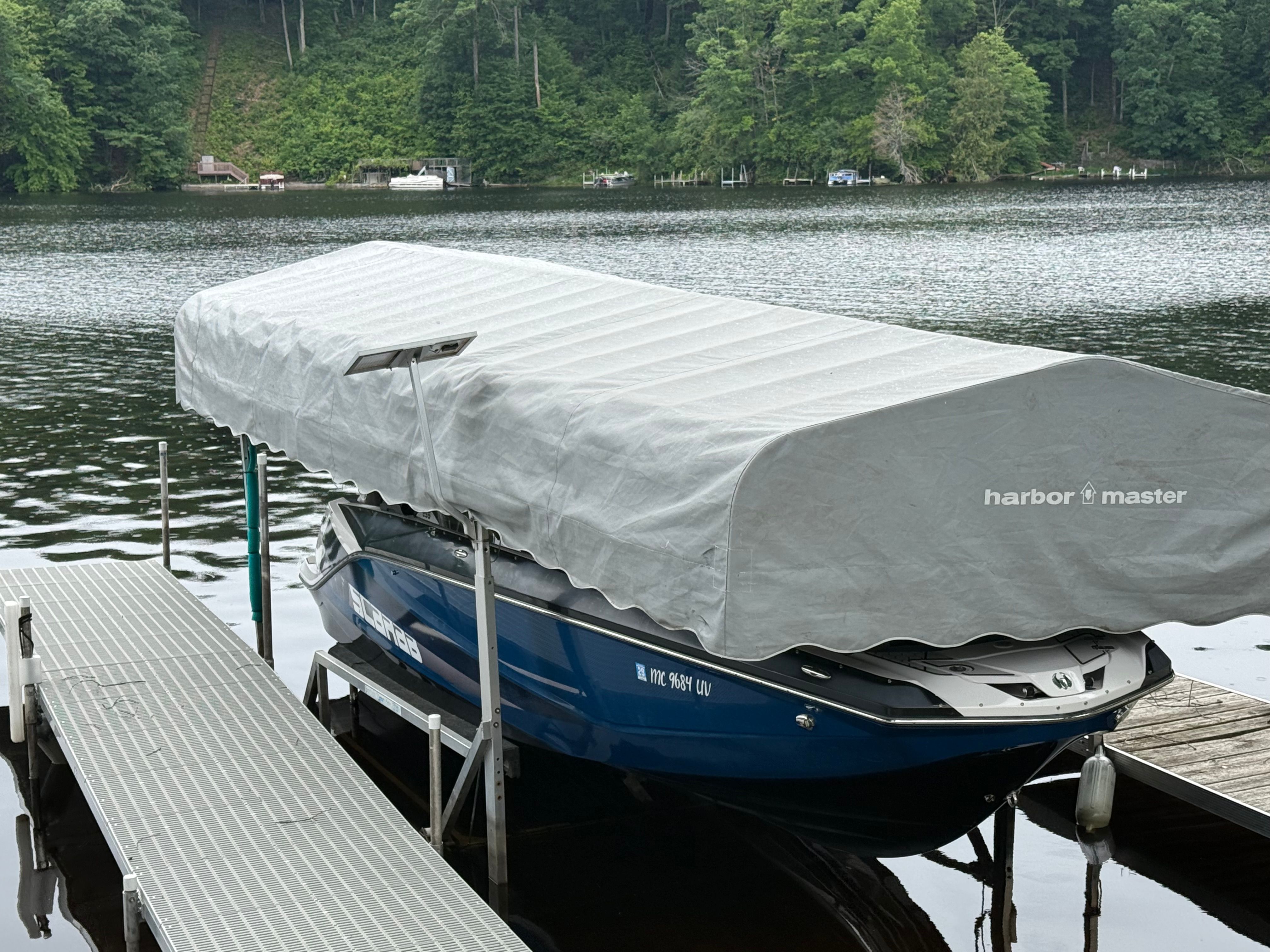 A 2018 Scarab 255 HOI is covered at a dock on a calm lake.