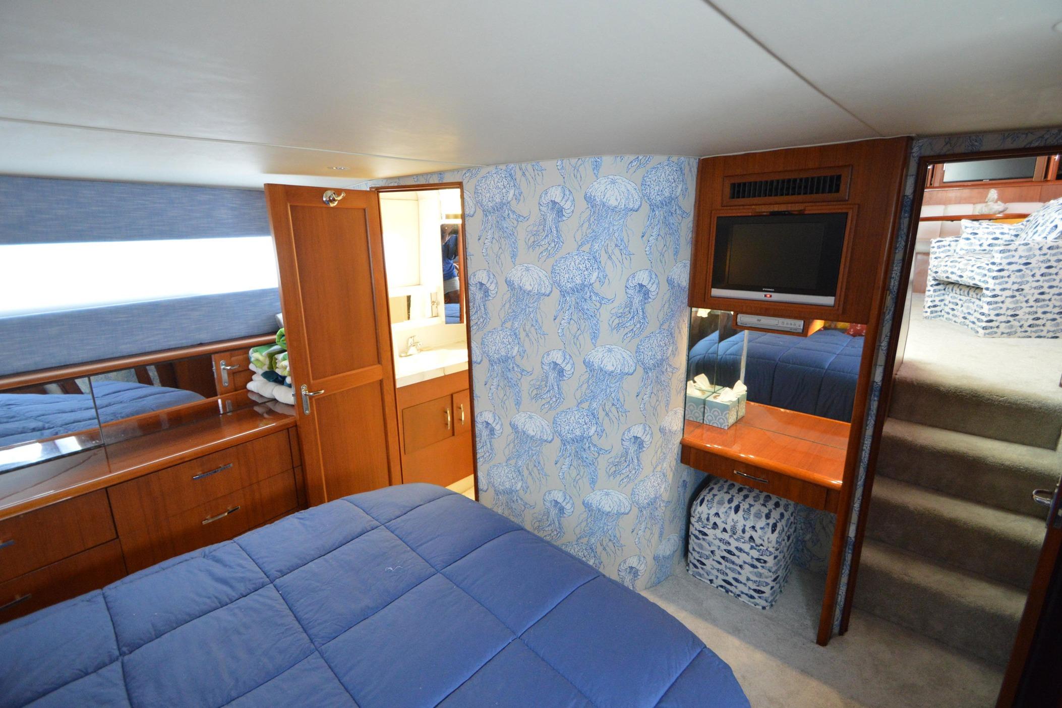 Luxurious 1995 Ocean 48 Cockpit Motor Yacht bedroom with blue bedding and wooden cabinetry.