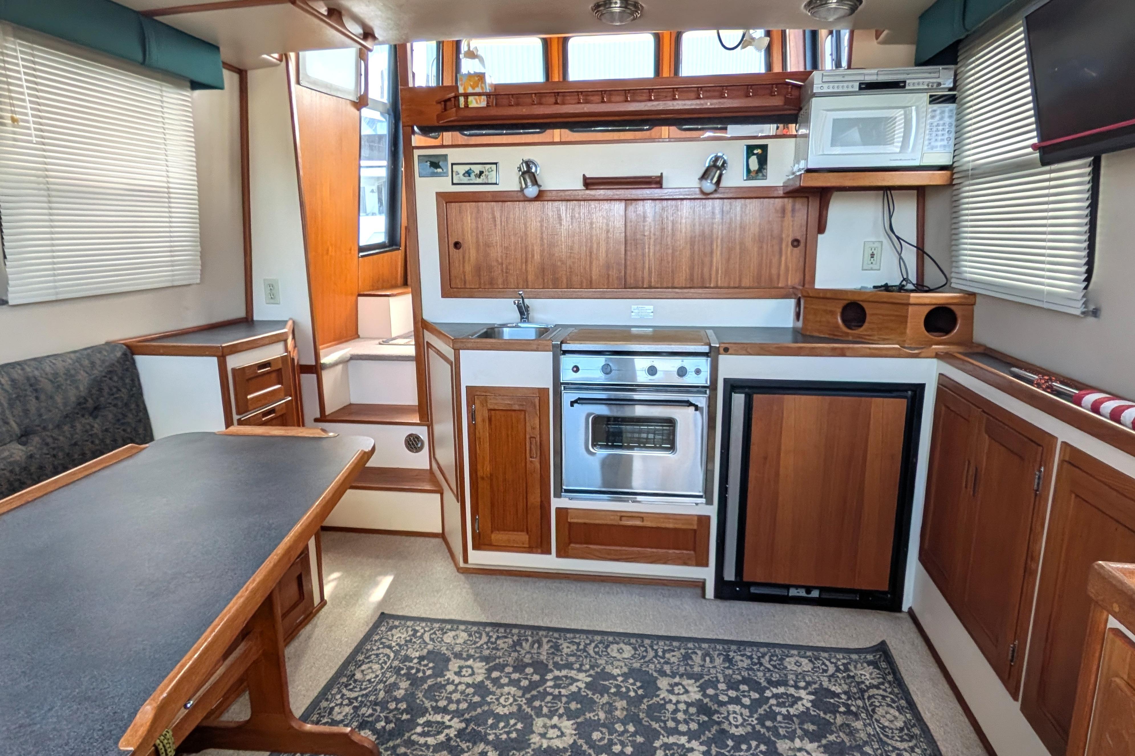 Cozy 1998 Nordic Tug 32 interior with kitchen, dining area, and wooden cabinetry.
