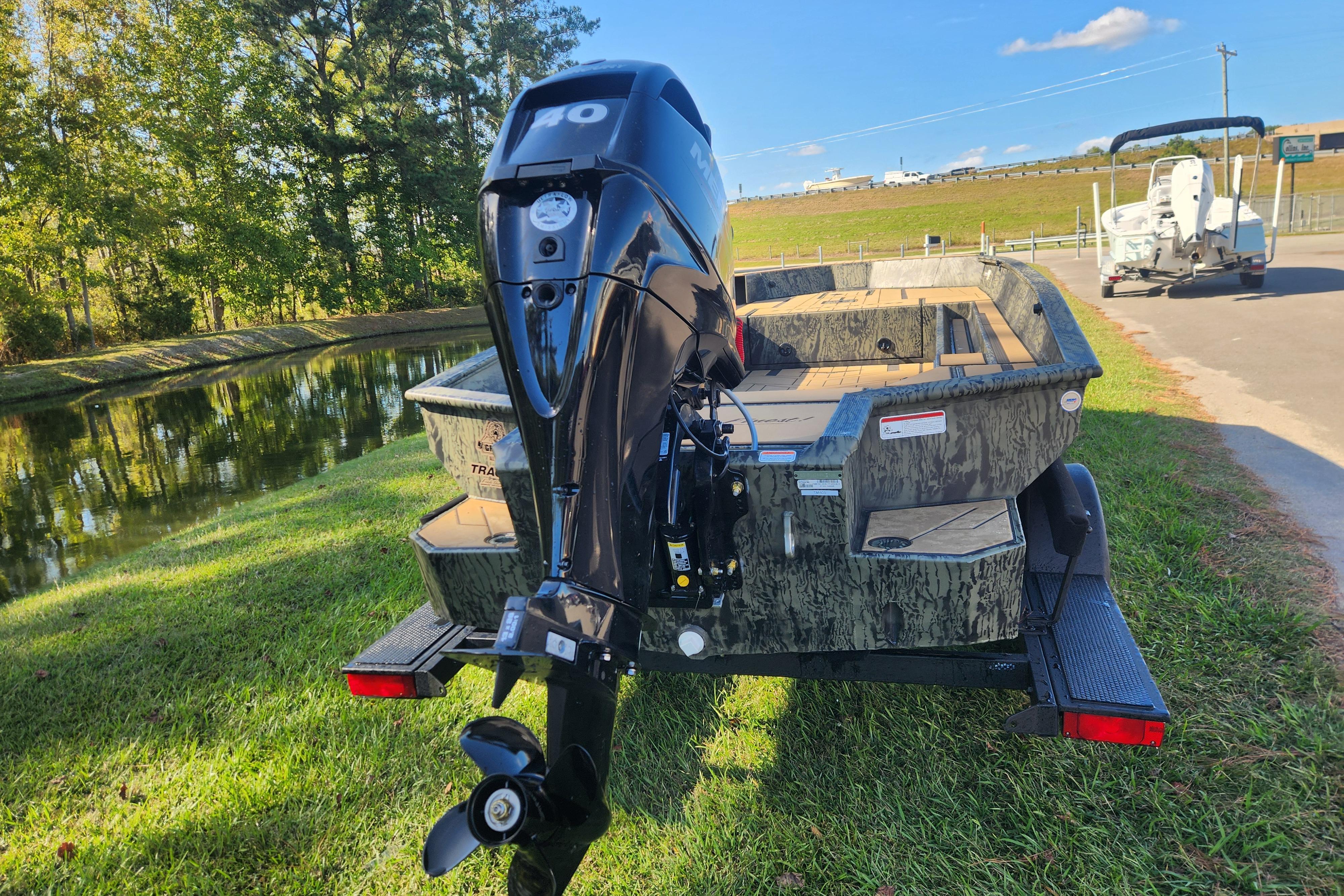 2026 Tracker Grizzly 1756 T Marsh boat with outboard motor on grassy area near water.